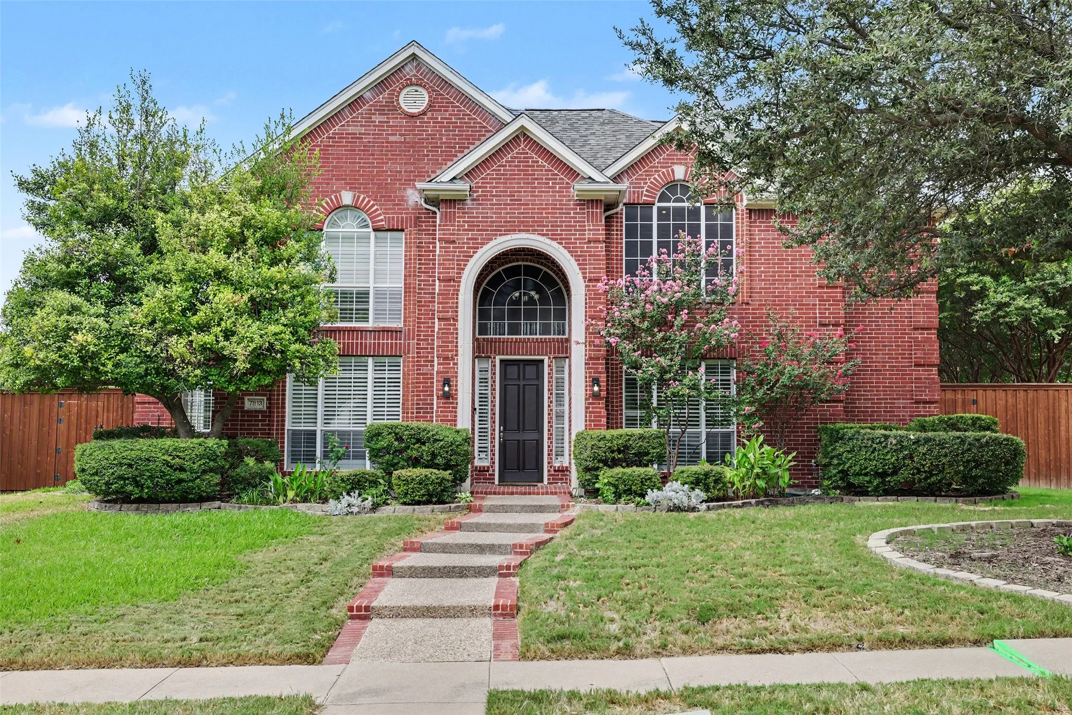 Traditional brick exterior with arched entryway, decorative front door, multiple arched windows, and mature landscaping