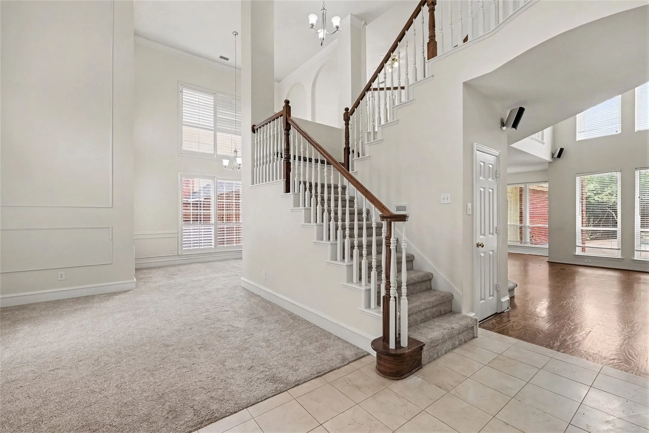 Two-story foyer featuring a grand staircase with wood railings, carpeted stairs, and tile flooring