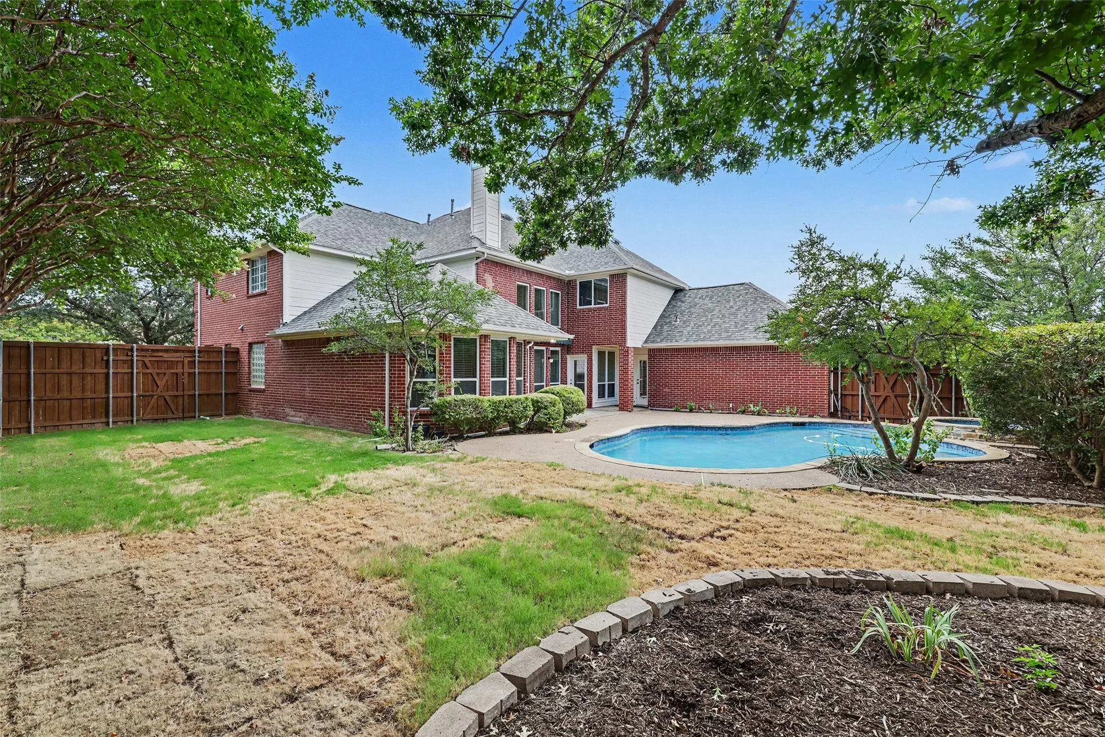 Brick exterior residence featuring a curved swimming pool, integrated spa, and an expansive concrete patio