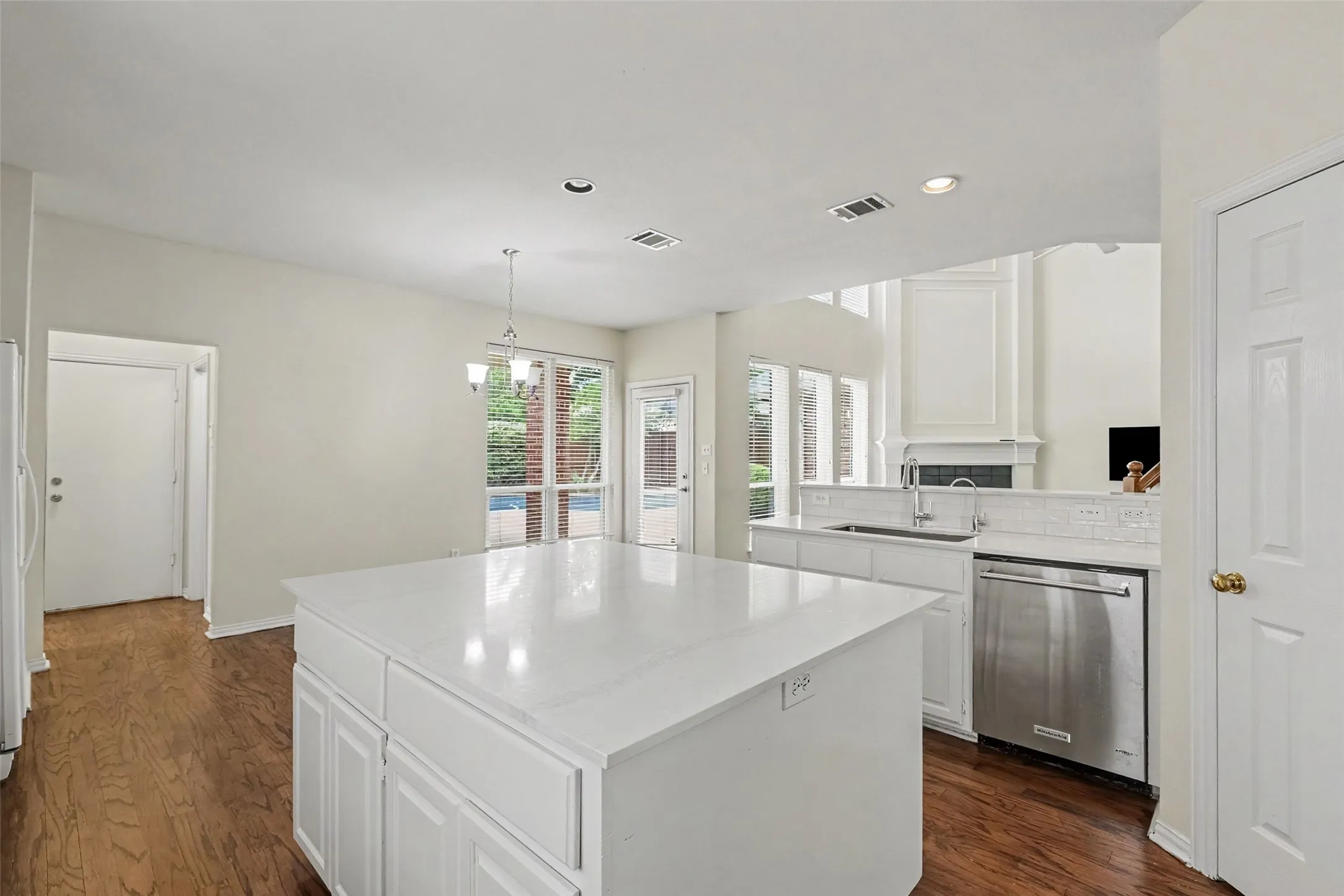 Kitchen featuring a large island with white countertops, white cabinetry, stainless steel dishwasher, and wood-finish flooring