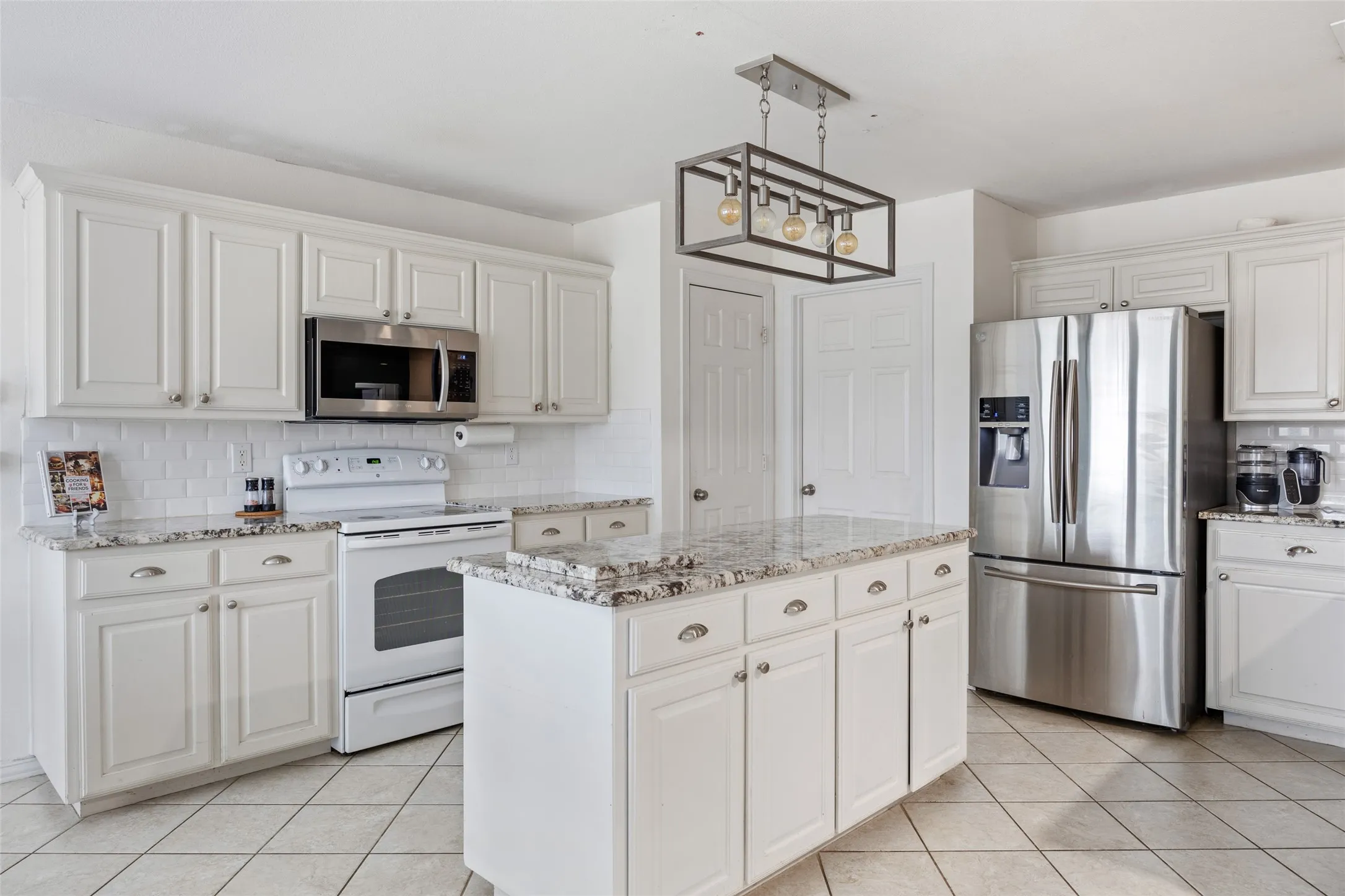 White cabinetry with brushed nickel hardware, granite countertops, tile flooring, stainless steel appliances, and a central island with storage