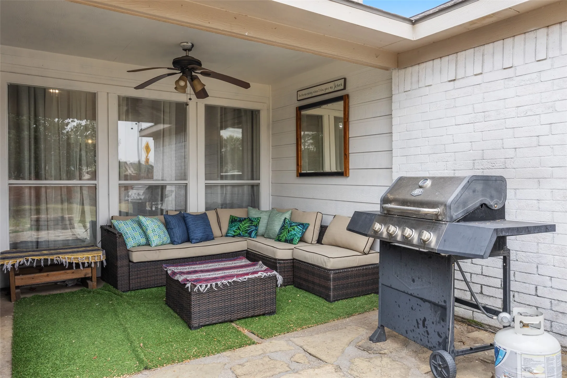 Covered patio with an outdoor ceiling fan, white brick exterior, and multiple windows