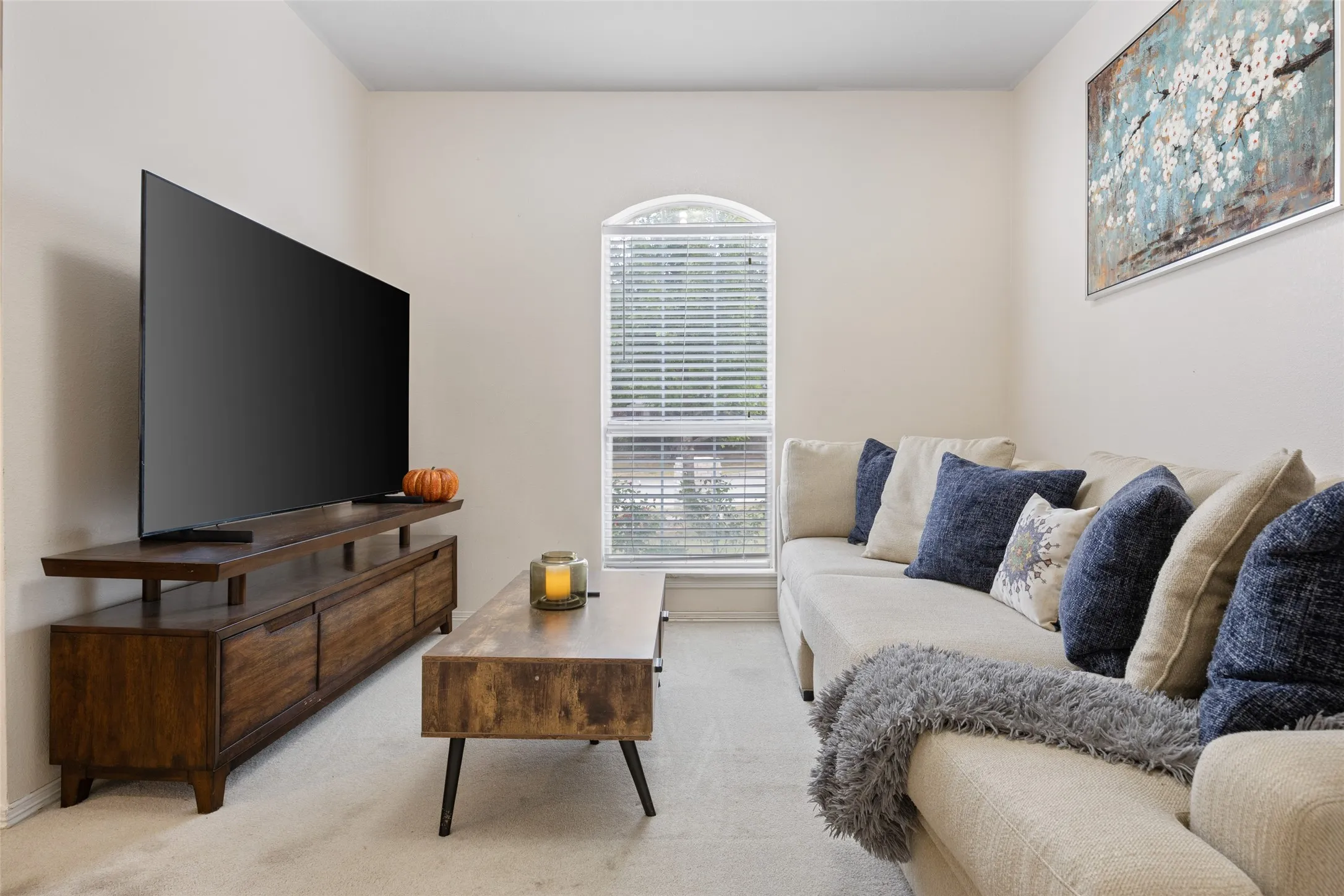 Neutral wall paint, arched window with blinds, and light-colored carpeting