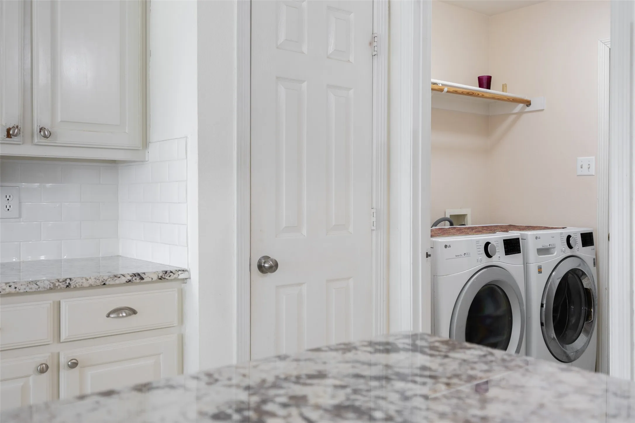 Granite-style countertops, white cabinetry, subway tile backsplash, and a dedicated laundry area with shelving