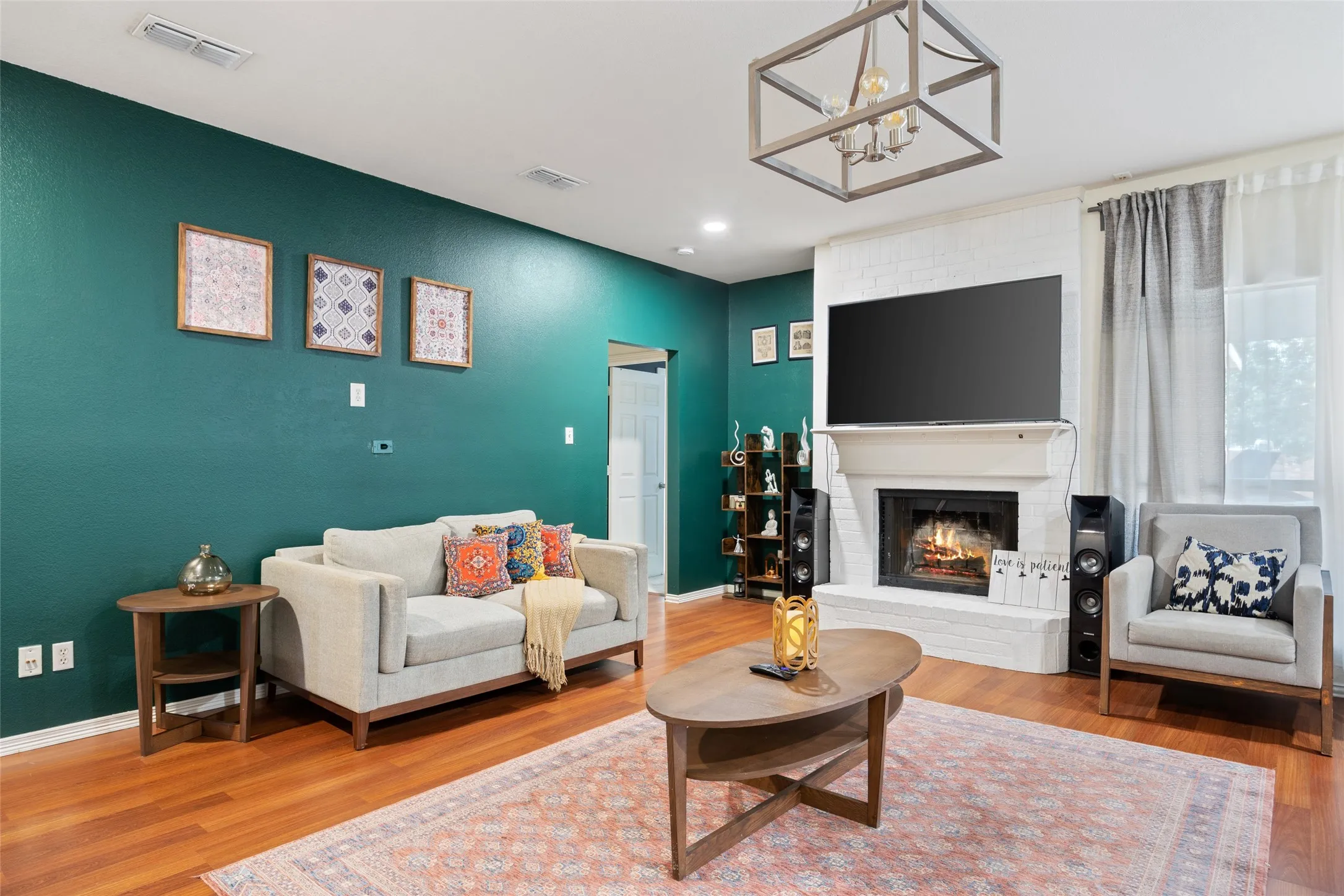 Living area featuring wood-finish flooring, a white brick fireplace with a mantel, and an open-frame chandelier