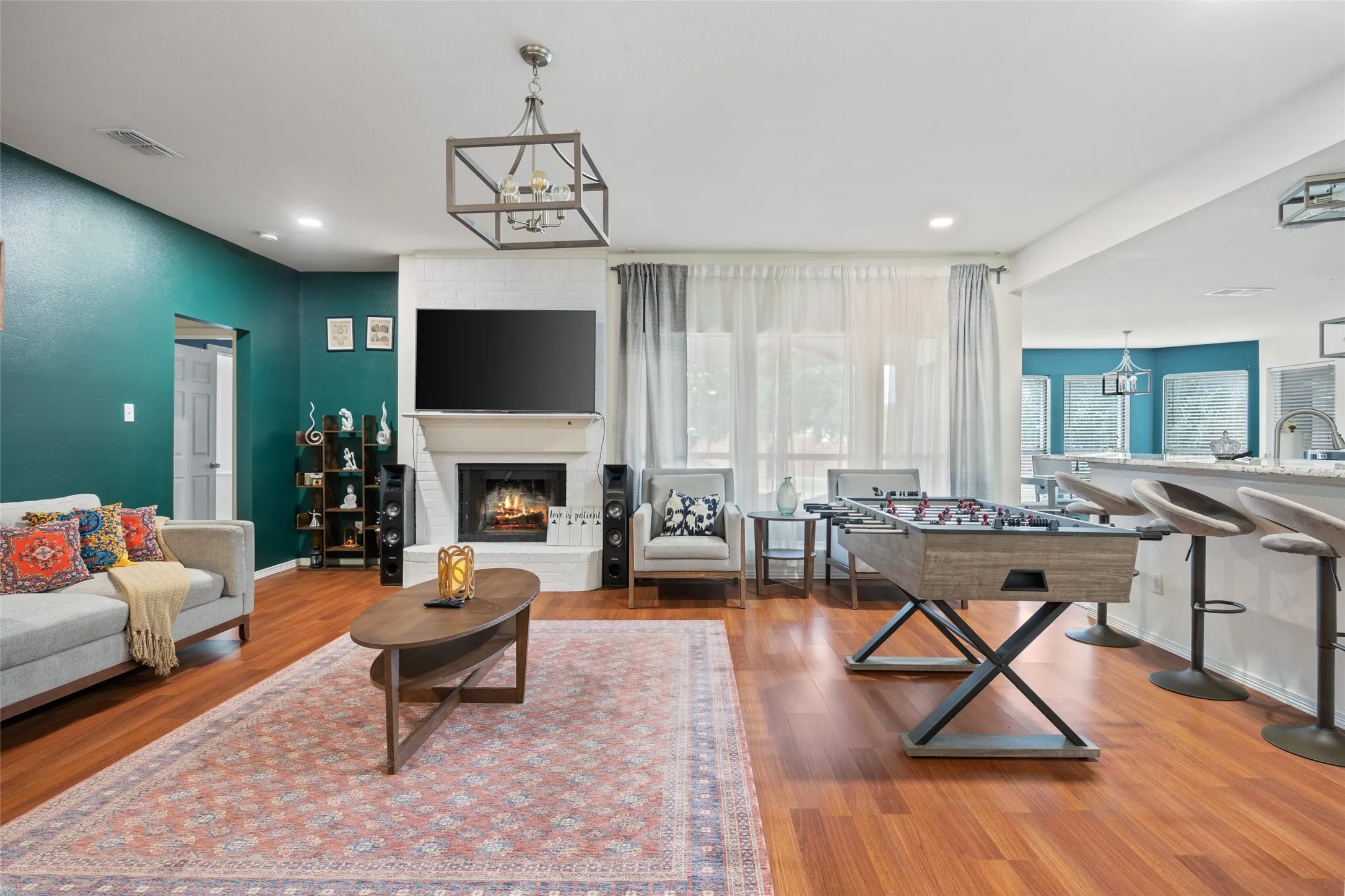 Open-concept living space with wood-finish flooring, a white brick fireplace, and a contemporary chandelier