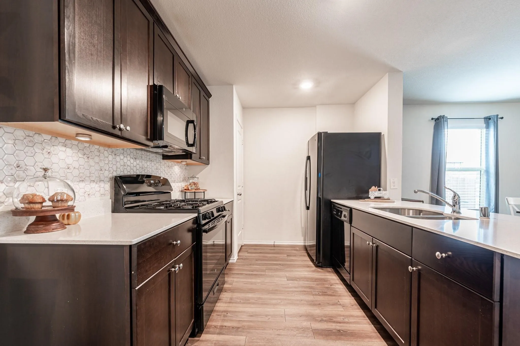 Kitchen with light wood-type flooring, black appliances, dark brown cabinets, sink, and tasteful backsplash