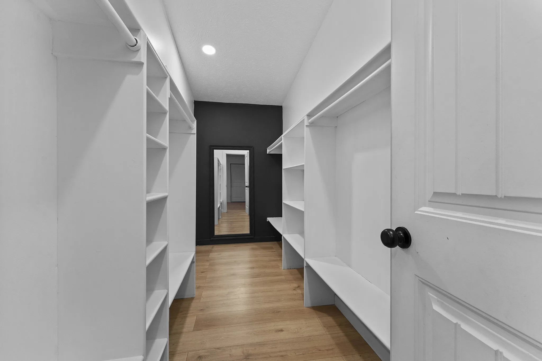 Spacious primary bedroom walk-in closet featuring abundant built-in shelving, multiple hanging areas, and a full-length mirror.