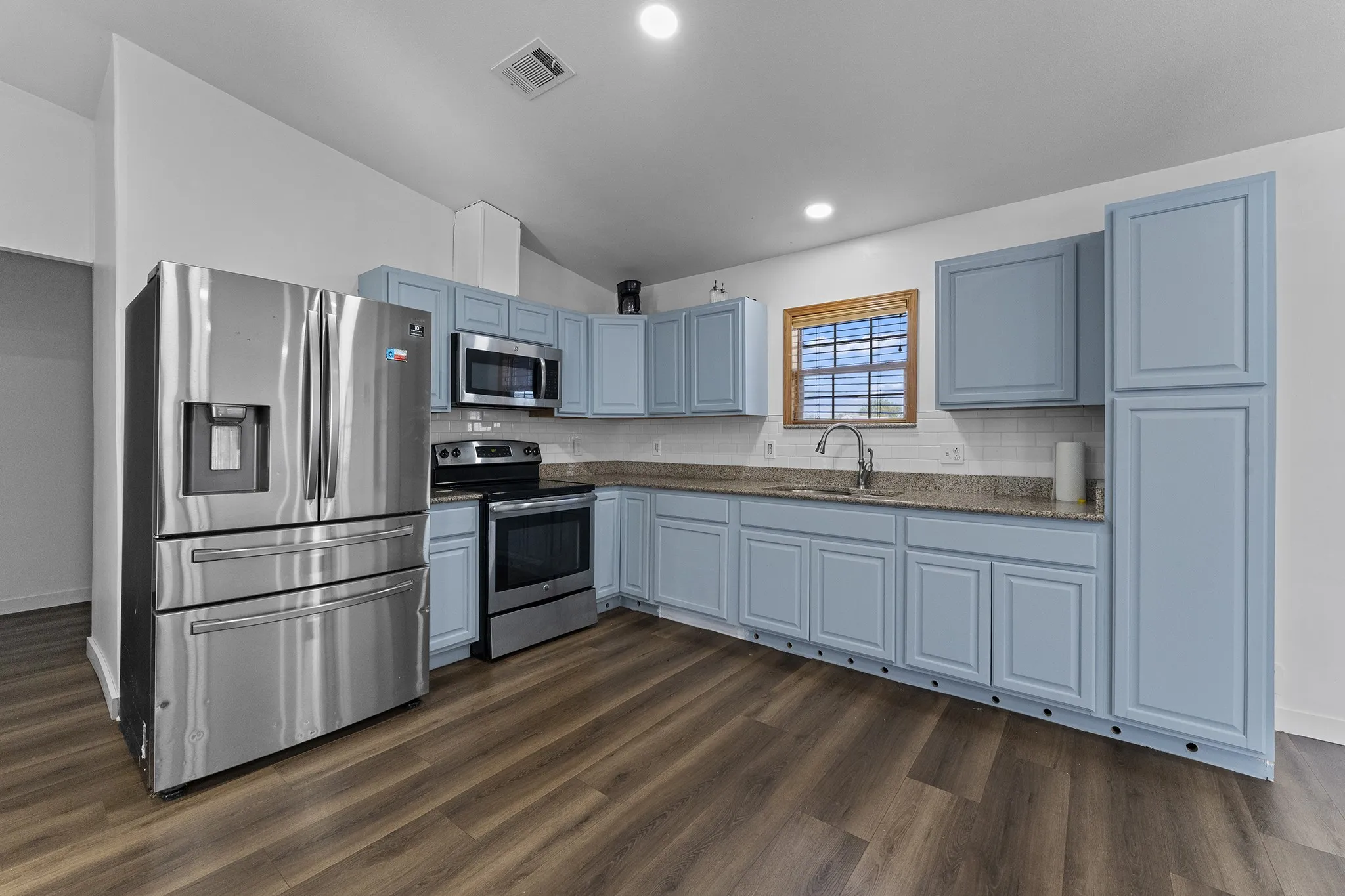 Bright, open kitchen featuring abundant cabinet and counter space, stainless-steel appliances, recessed lighting, and wood-look flooring.