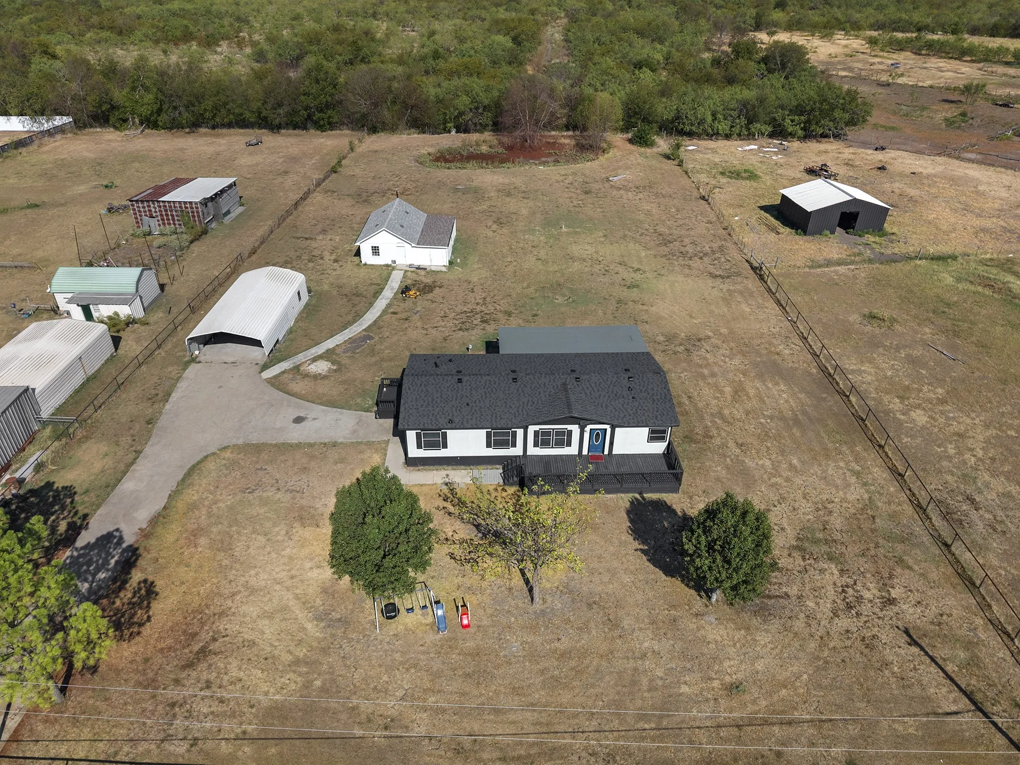Aerial view showcasing the expansive fenced acreage, main residence, circular driveway, and multiple detached outbuildings offering additional storage or workspace.