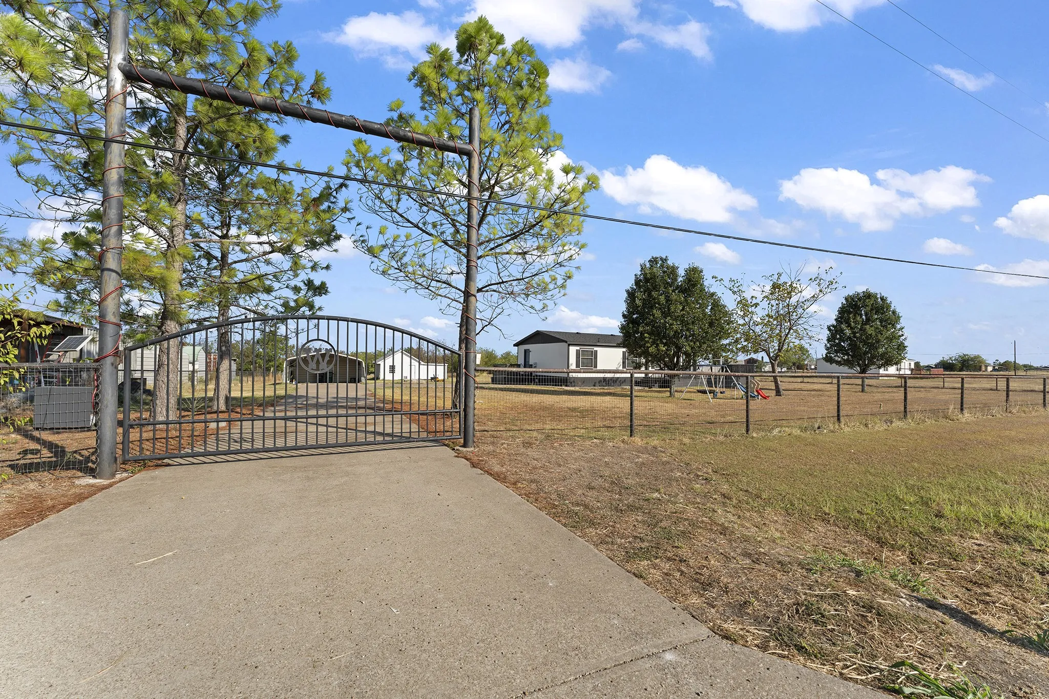 Gated property entrance featuring a decorative metal gate, perimeter fencing, and a concrete driveway.