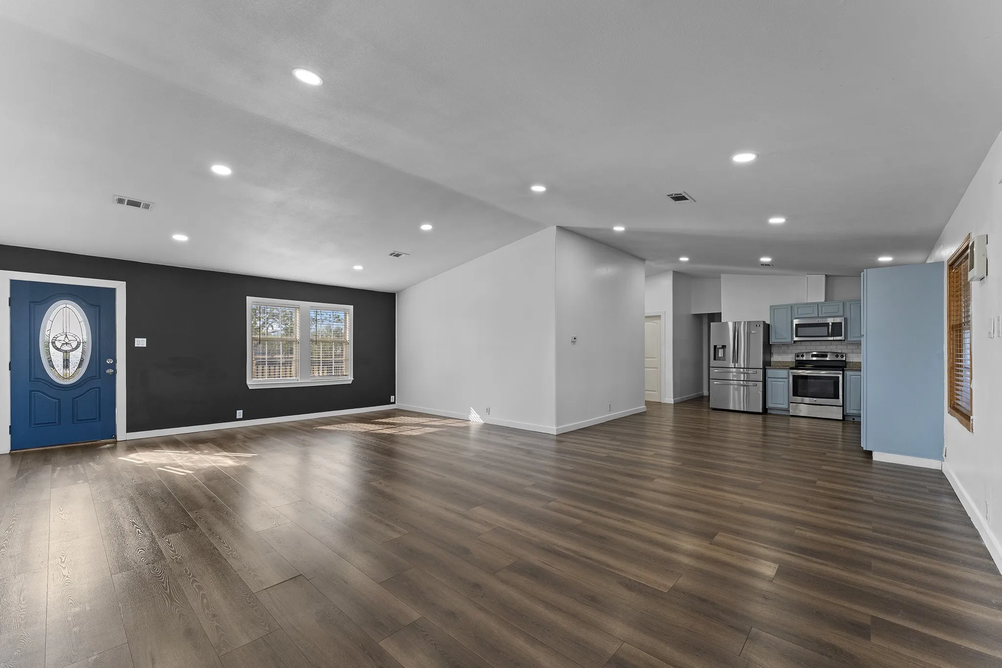Spacious open-concept living, dining, and kitchen area featuring wood-look flooring, recessed lighting, and stainless-steel appliances.