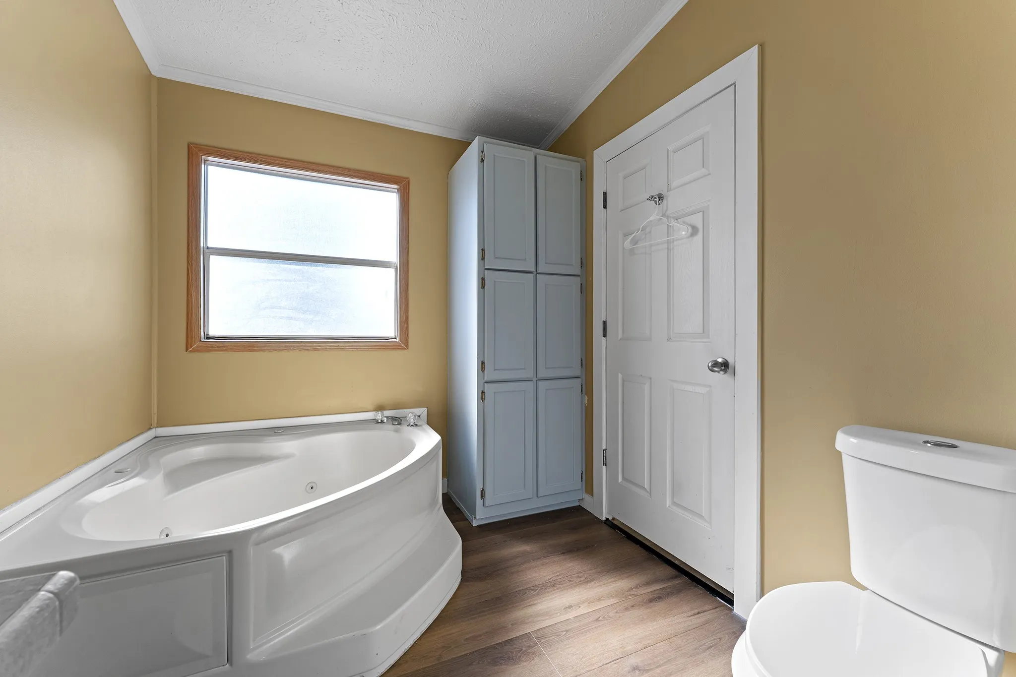 Spacious primary bathroom featuring a relaxing corner soaking tub, natural light, and convenient built-in storage.