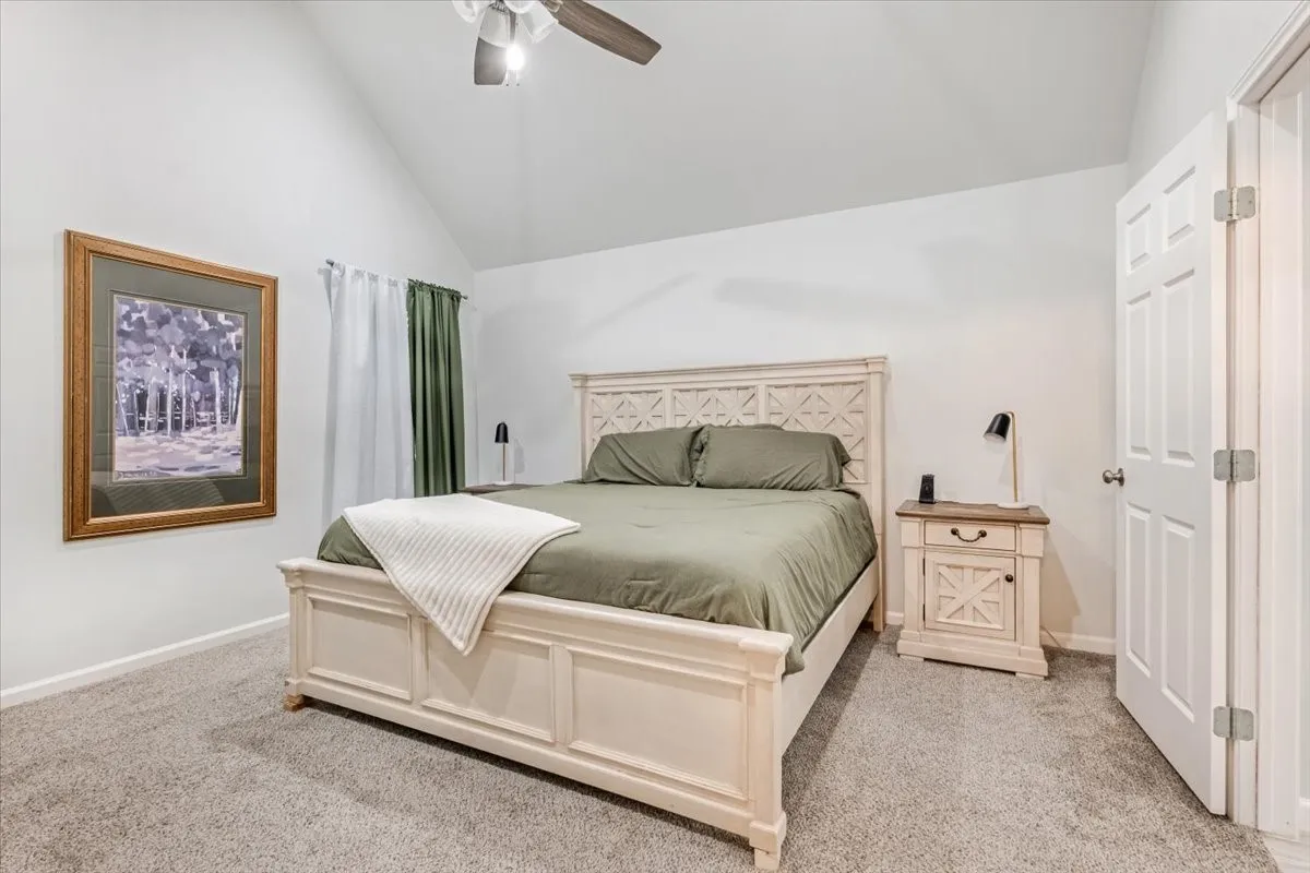 Vaulted ceiling, ceiling fan, neutral carpeting, paneled door, and window with curtain rod