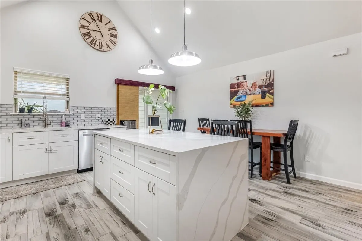 Vaulted ceiling, white shaker cabinetry, stainless steel dishwasher, white subway tile backsplash, wood-finish flooring