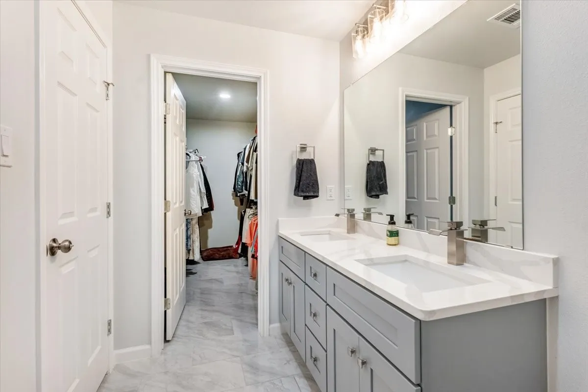 Dual vanity with undermount sinks, stone countertops, gray cabinetry, and brushed nickel fixtures