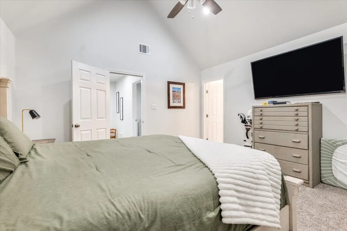 Vaulted ceiling, ceiling fan, carpet flooring, wall-mounted television, and a paneled door