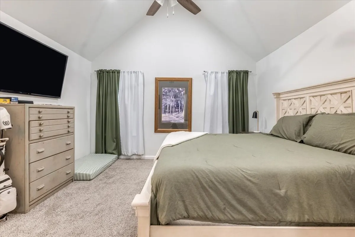 Vaulted ceiling with a ceiling fan, carpeted flooring, and two windows