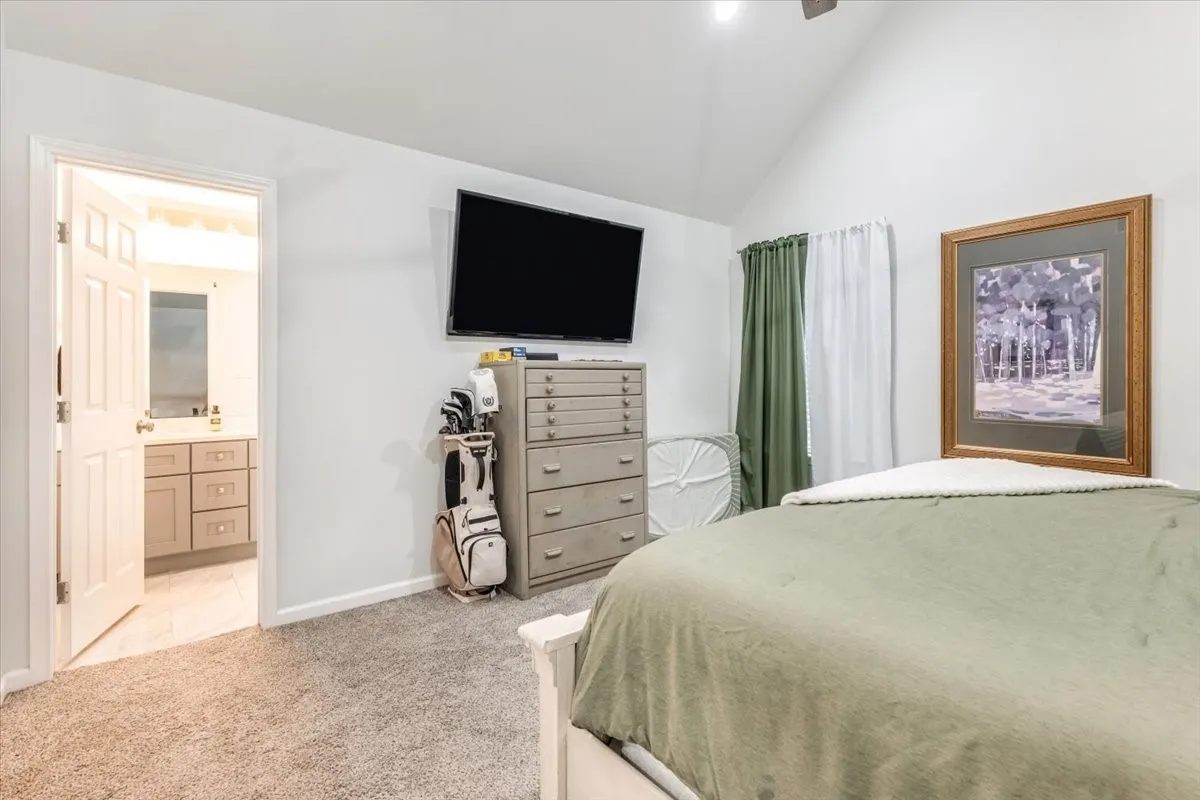 Vaulted ceiling bedroom with carpet flooring and direct access to a bathroom featuring a vanity with storage