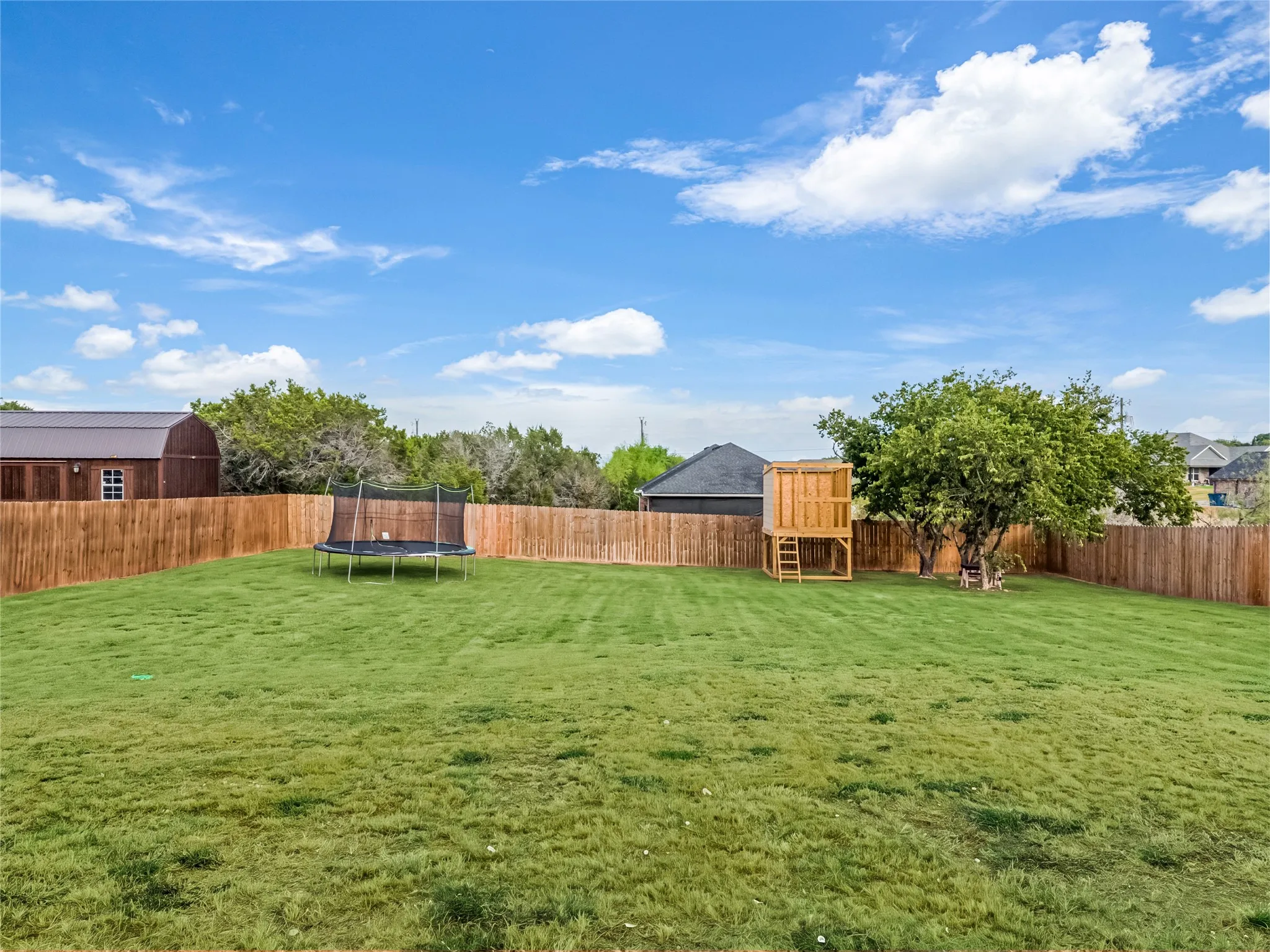 Expansive backyard featuring a manicured lawn, full privacy fencing, and mature trees