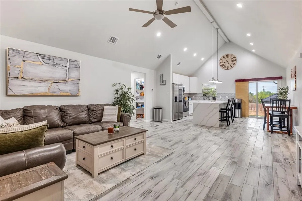 Vaulted ceiling with recessed lighting, wood-finish flooring, kitchen island with seating, stainless steel appliances, and sliding glass door
