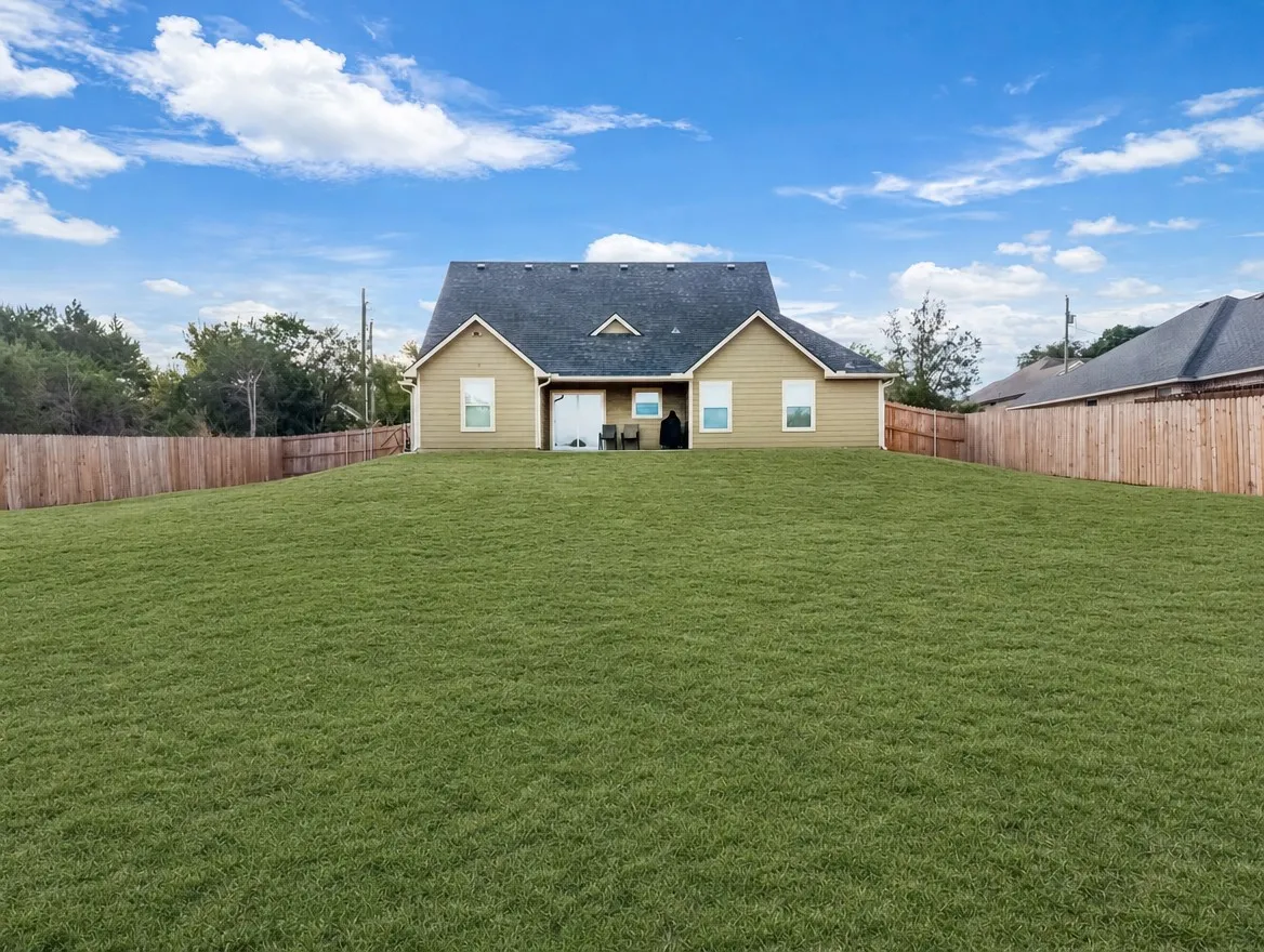 Expansive grassy yard with wood fencing, featuring a two-story home with light-colored siding and a dark roof