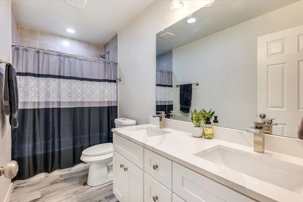 Dual vanity with integrated sinks, brushed nickel fixtures, a full-width mirror, and wood-finish flooring