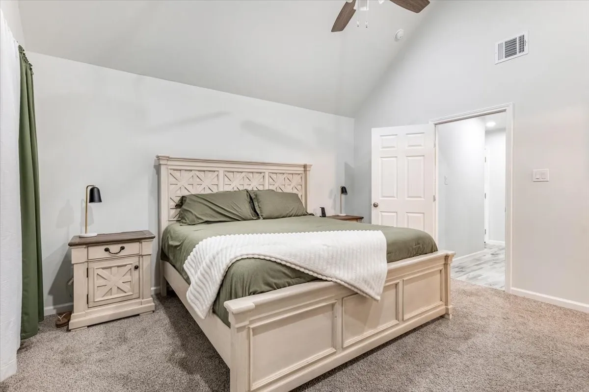 Vaulted ceiling with an installed ceiling fan, carpeted flooring, and a paneled interior door