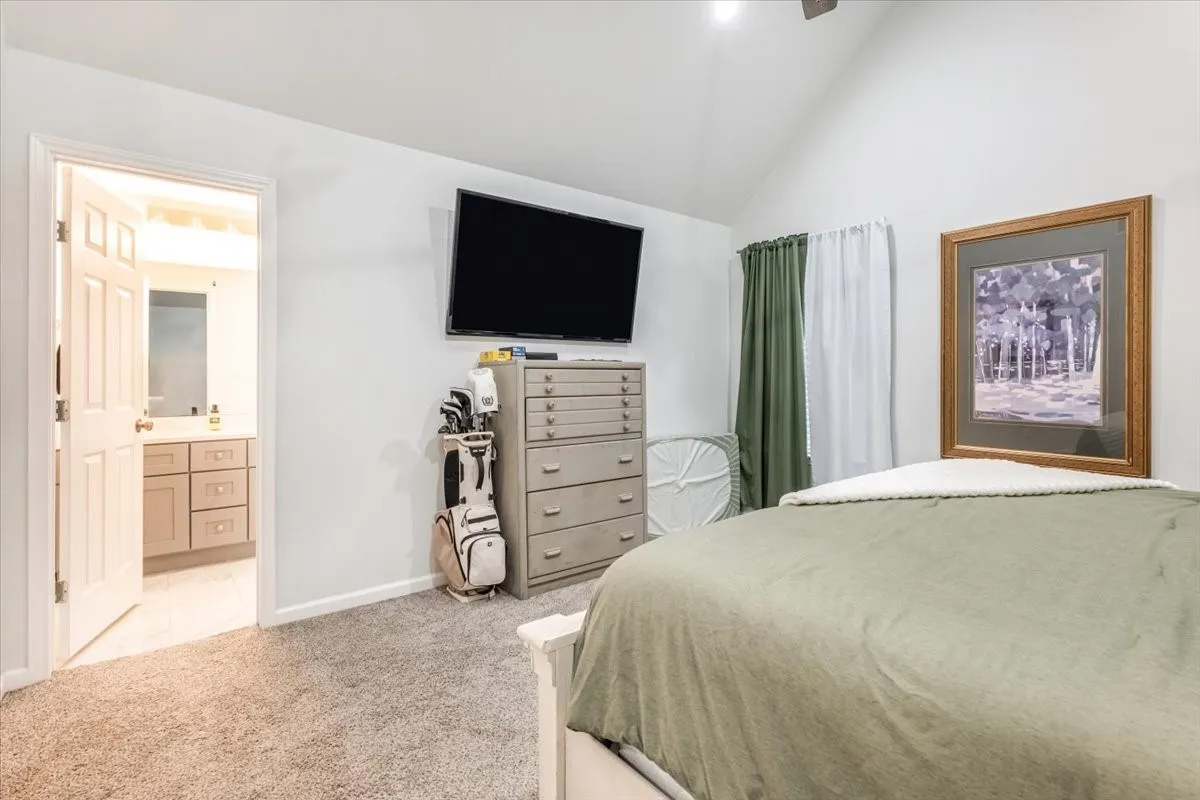 Vaulted ceiling with ceiling fan, carpeted flooring, and an open doorway leading to a bathroom featuring a vanity with an undermount sink