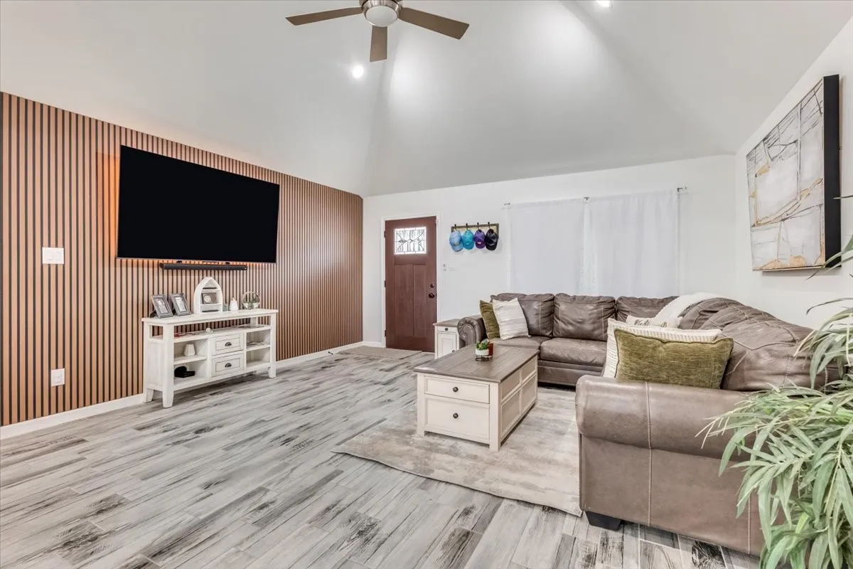 Vaulted ceiling, wood-finish flooring, wood accent wall, recessed lighting, and a ceiling fan