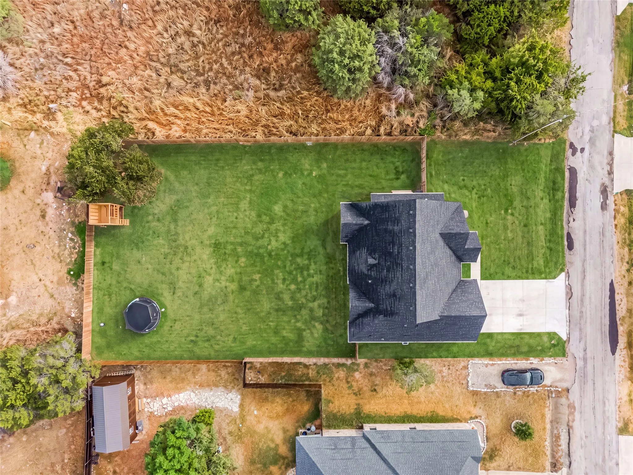Expansive grassy lawn with a privacy fence, wood deck, and detached shed