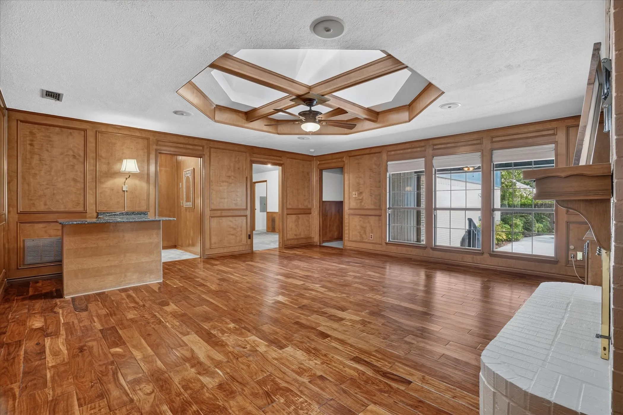 Living room with gorgeous wood floors, a unique skylight, and large windows with views to the backyard and pool