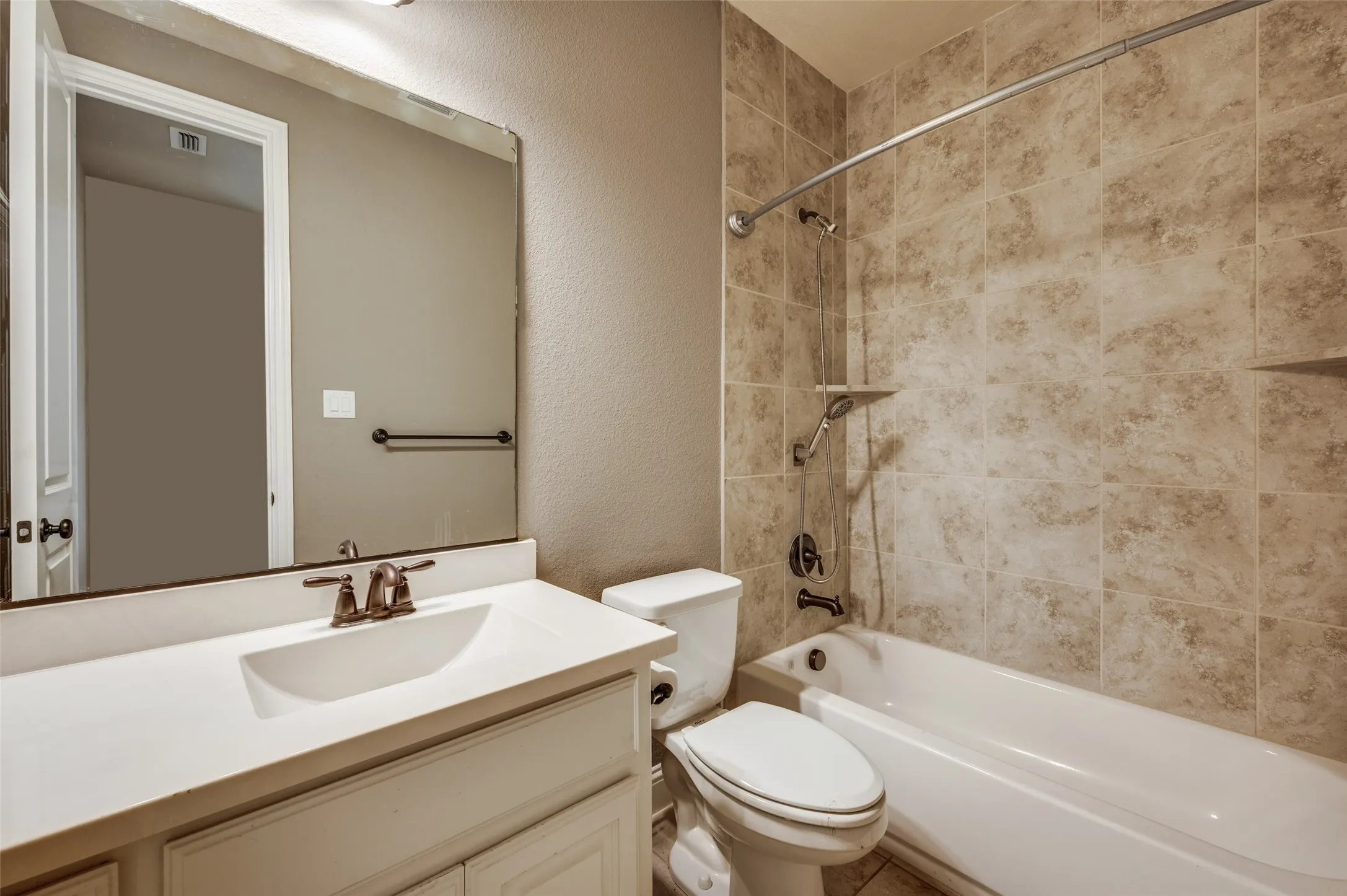 Bathroom featuring a white vanity with an integrated sink and bronze-finish faucet, a large frameless mirror, a shower-over-tub combination with tile surround, and an integrated tiled shelf