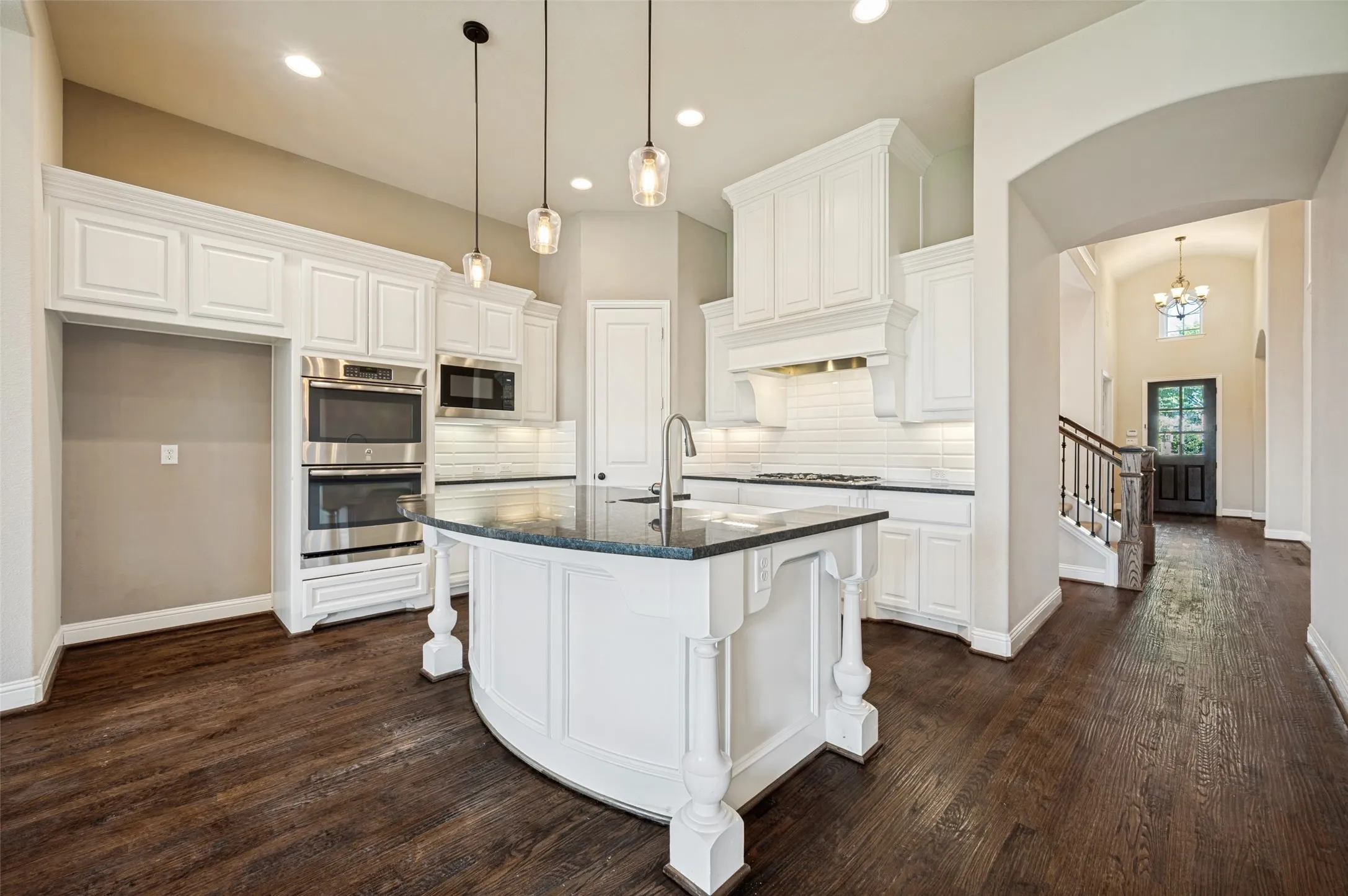 Contemporary kitchen featuring white cabinetry, stainless steel double ovens, a built-in microwave, and a contrasting dark countertop island with pendant lighting