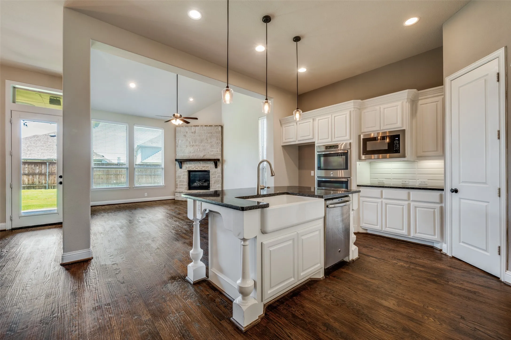 Kitchen featuring white cabinetry, dark countertops, a farmhouse sink, stainless steel appliances, and a tile backsplash