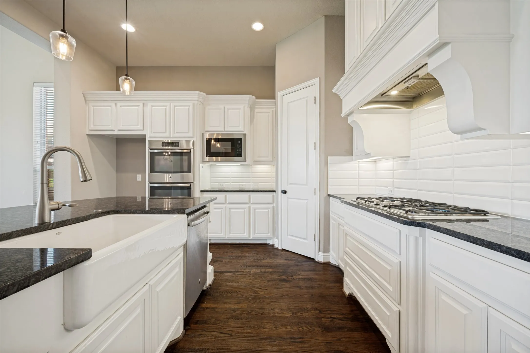 Kitchen featuring white cabinetry, dark stone countertops, stainless steel appliances, a farmhouse sink, and wood-finish flooring