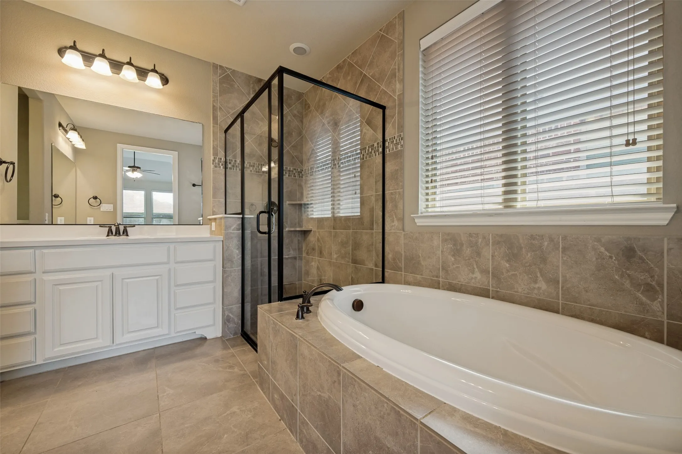 Tiled bathroom featuring a built-in soaking tub, glass-enclosed shower with tiled walls, and a double vanity with white cabinetry