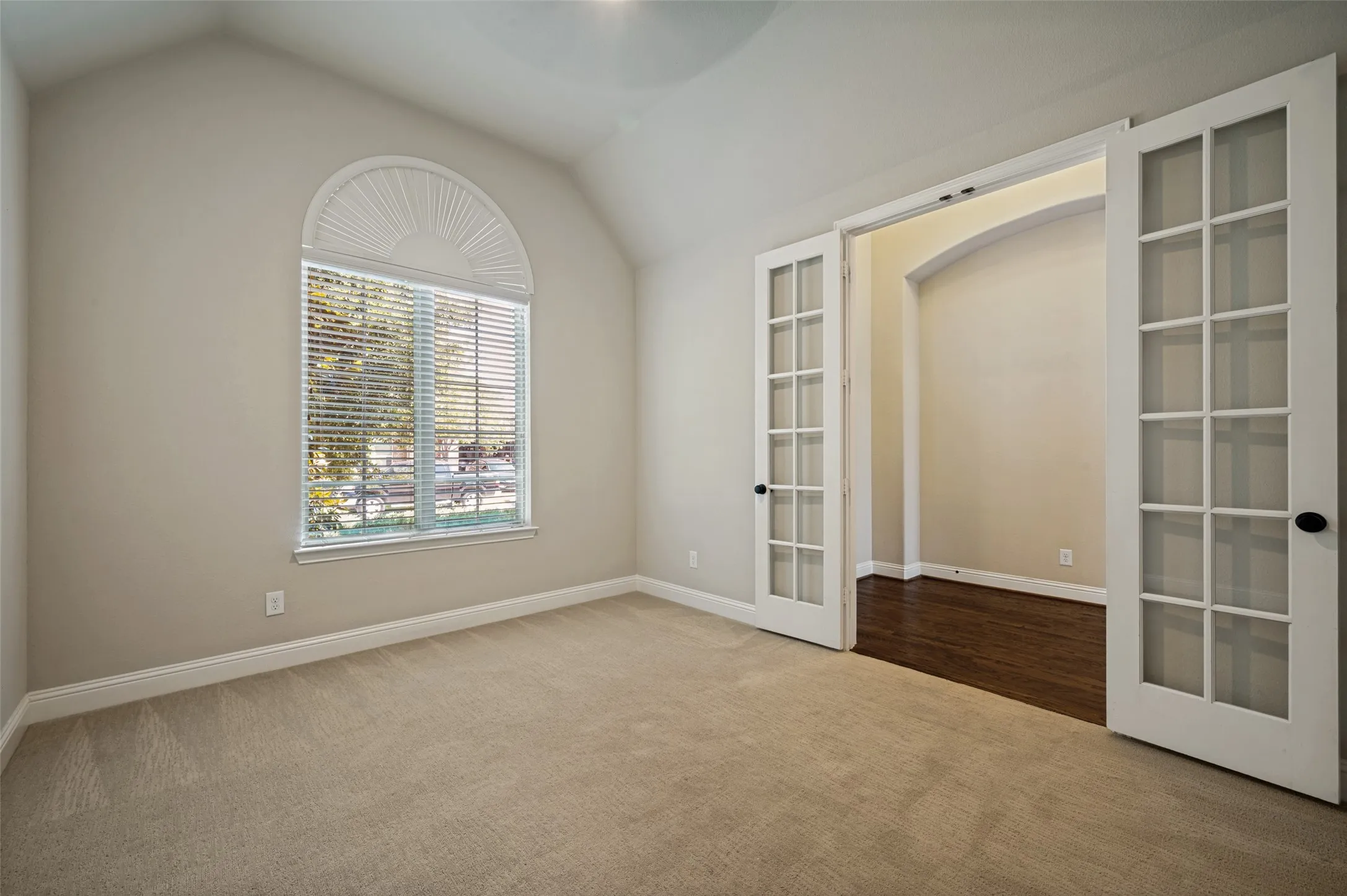Neutral-toned room featuring a large arched window with horizontal blinds, providing natural illumination