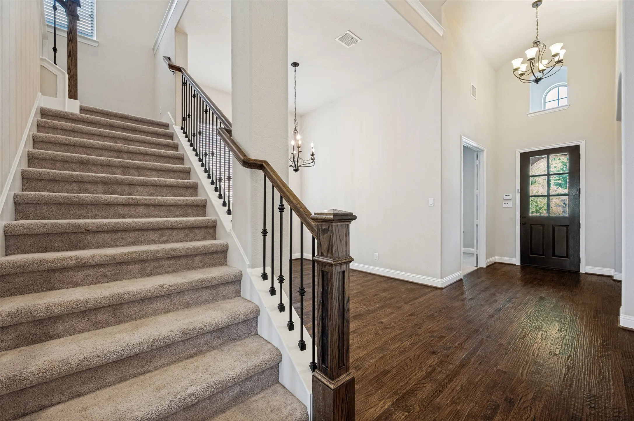 Carpeted staircase with dark wood handrail and iron balusters