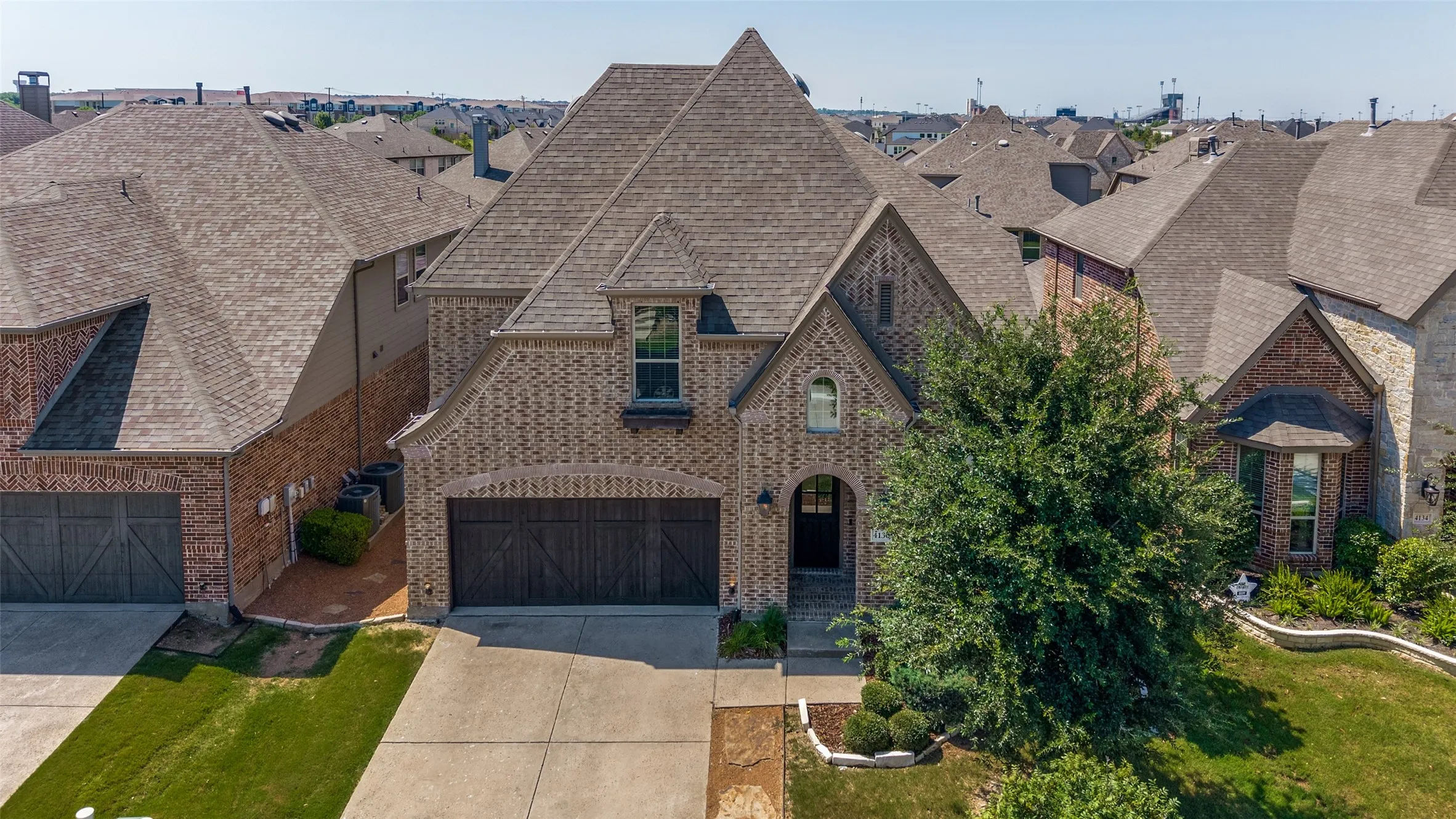 Brick facade residence with a pitched roofline, prominent gables, an arched entryway, and dark-stained garage doors