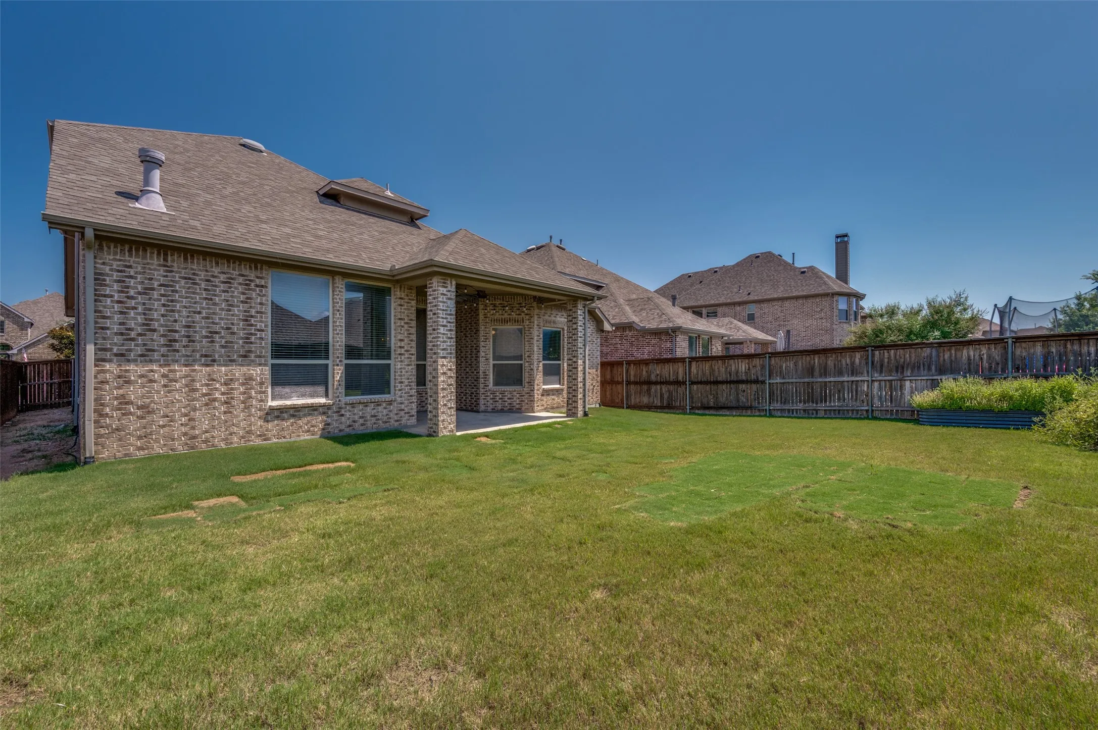 Expansive backyard featuring a covered patio, brick exterior, full privacy fencing, and a raised garden bed