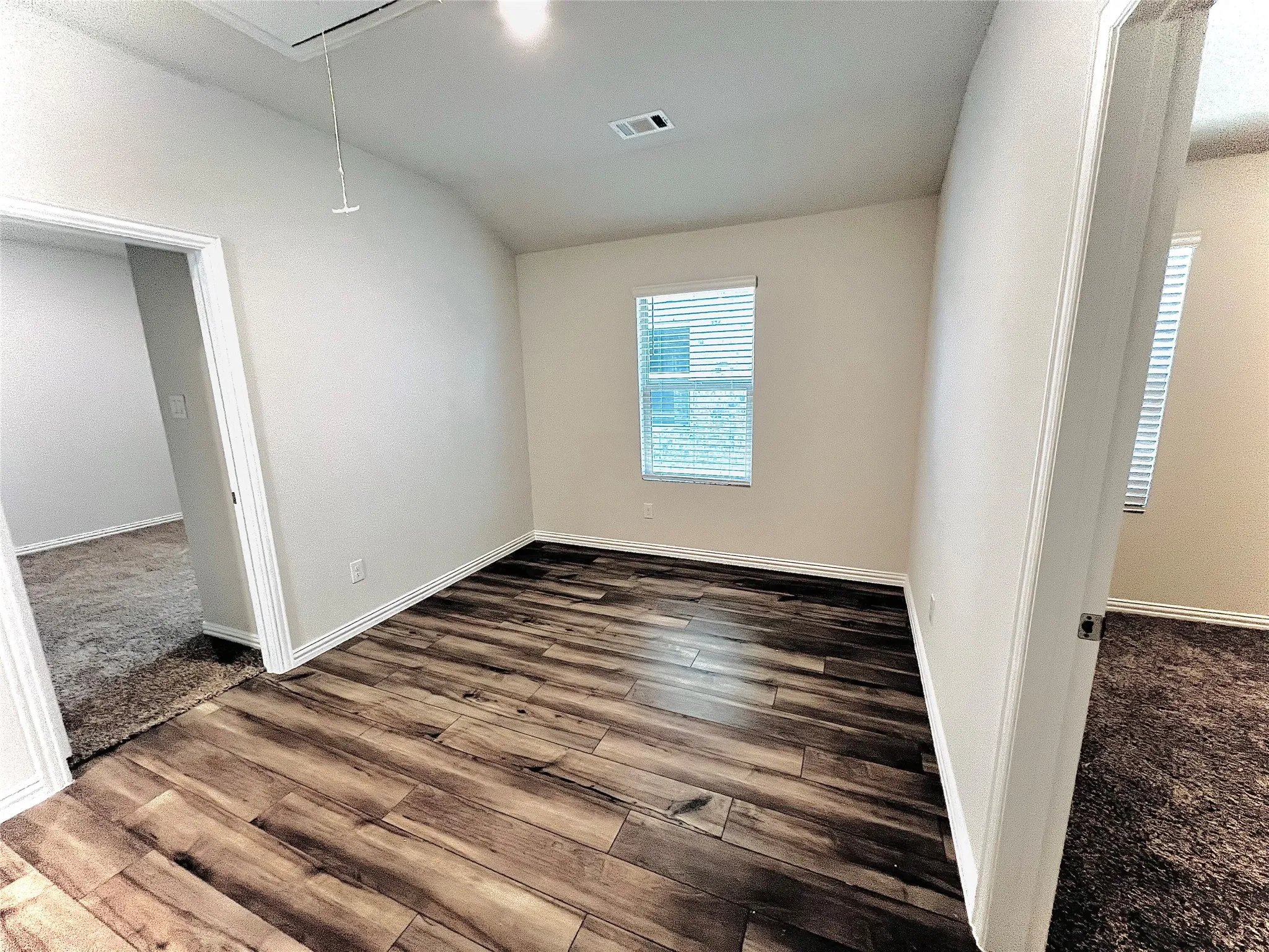 Wood-finish flooring, white trim, and a window with blinds