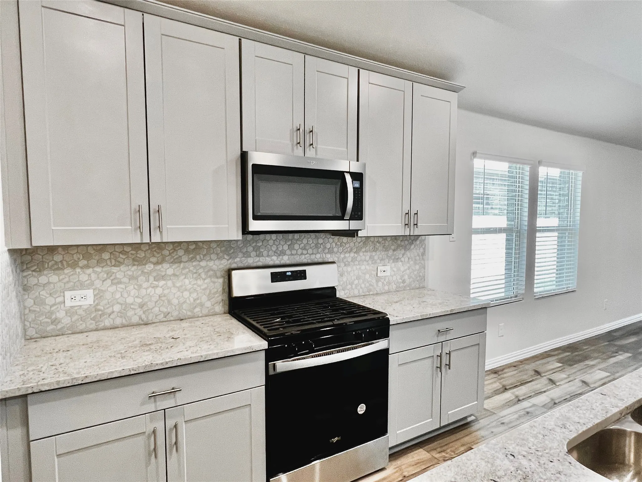Kitchen featuring light gray cabinetry, stainless steel appliances, stone countertops, and a mosaic tile backsplash