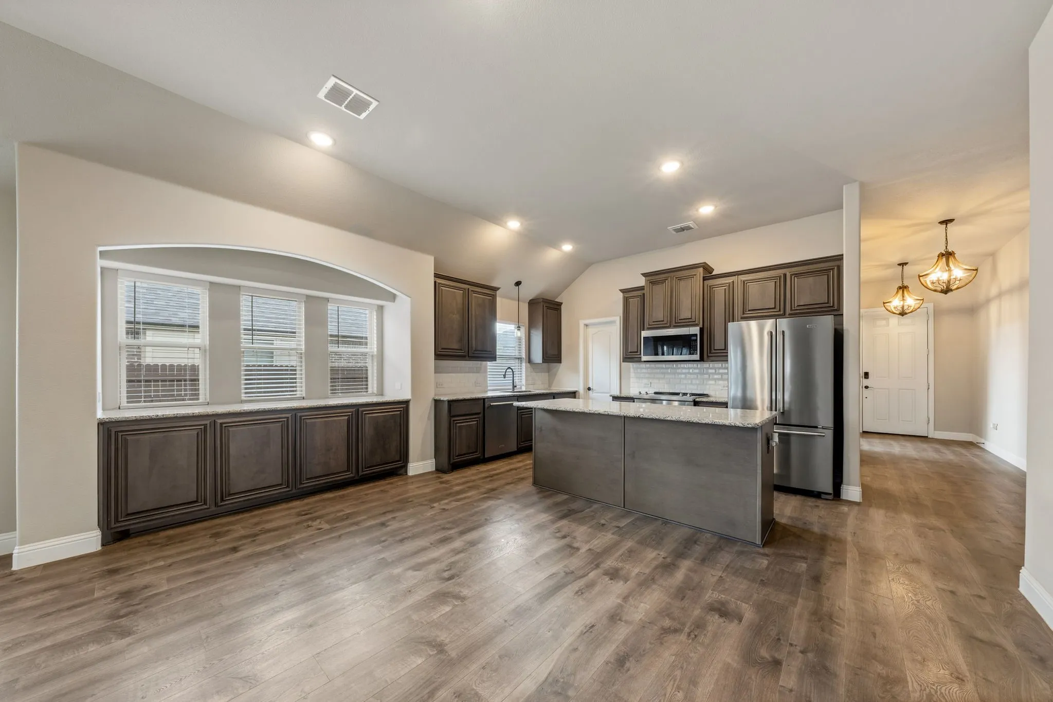 Open-concept kitchen featuring an island with stone countertops, stainless steel appliances, dark wood-finish cabinetry, and wood-finish flooring