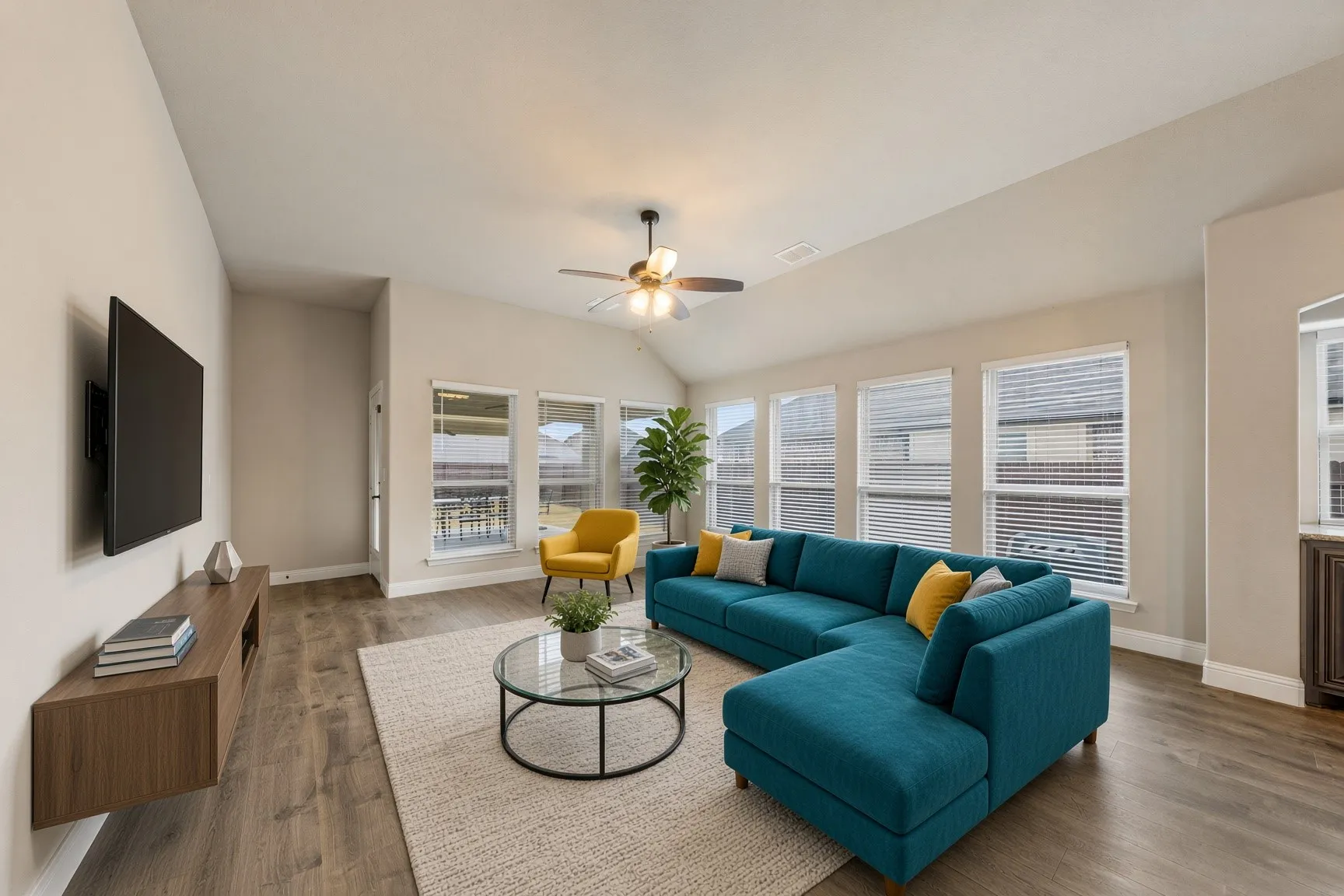 Vaulted ceiling with a ceiling fan, multiple windows with blinds, wood-finish flooring, and light-colored walls