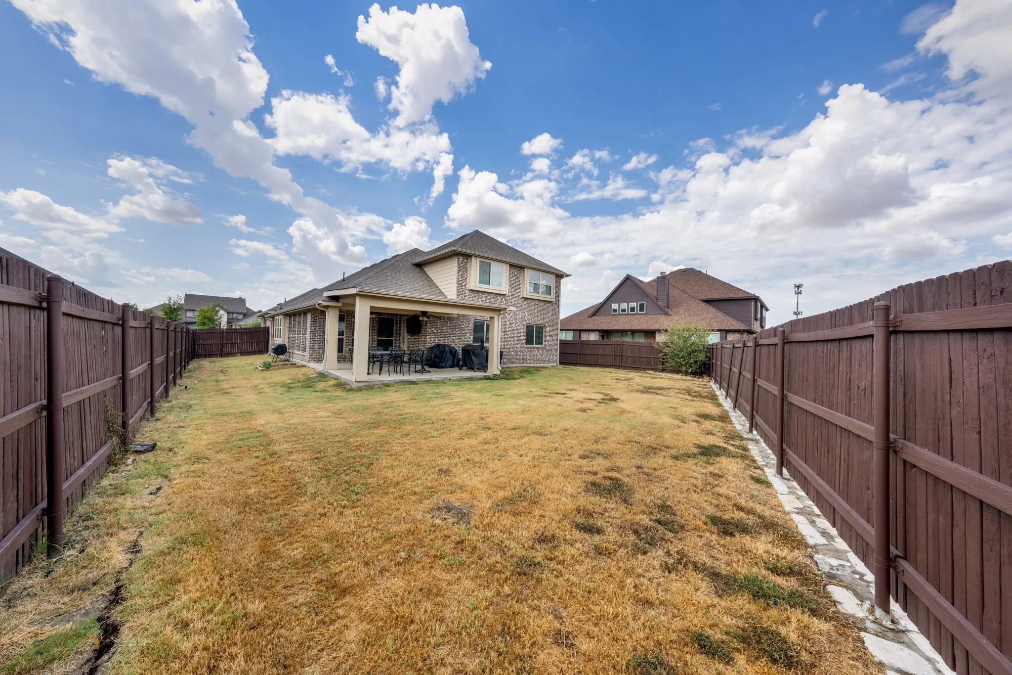 Expansive backyard featuring a covered patio with recessed lighting, brick exterior, and a privacy fence