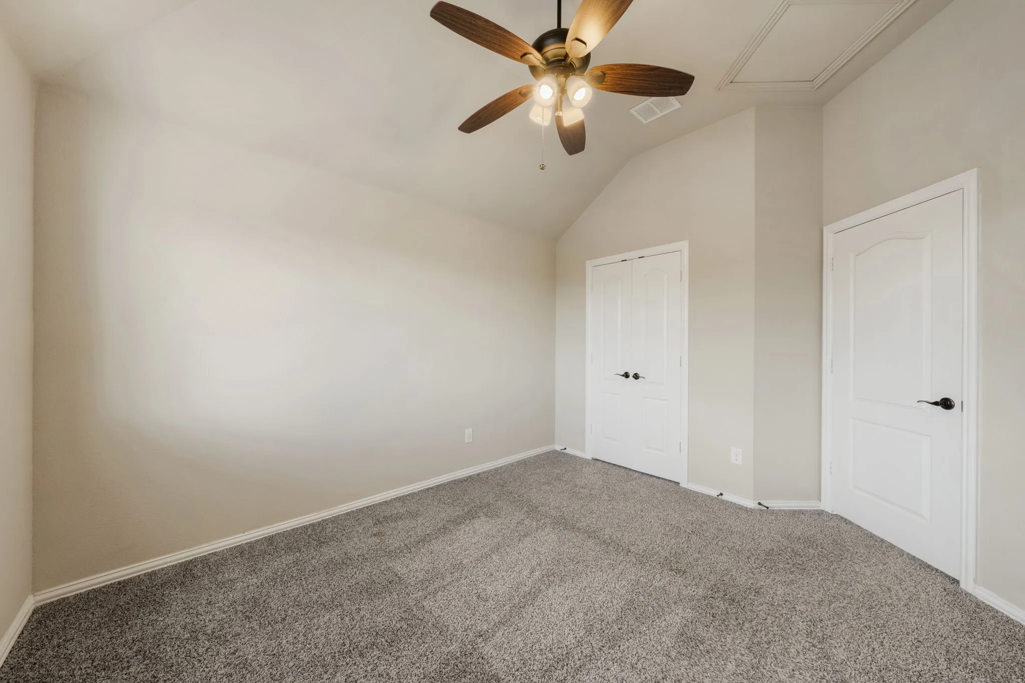 Vaulted ceiling with a ceiling fan, light-colored walls, and gray carpeting