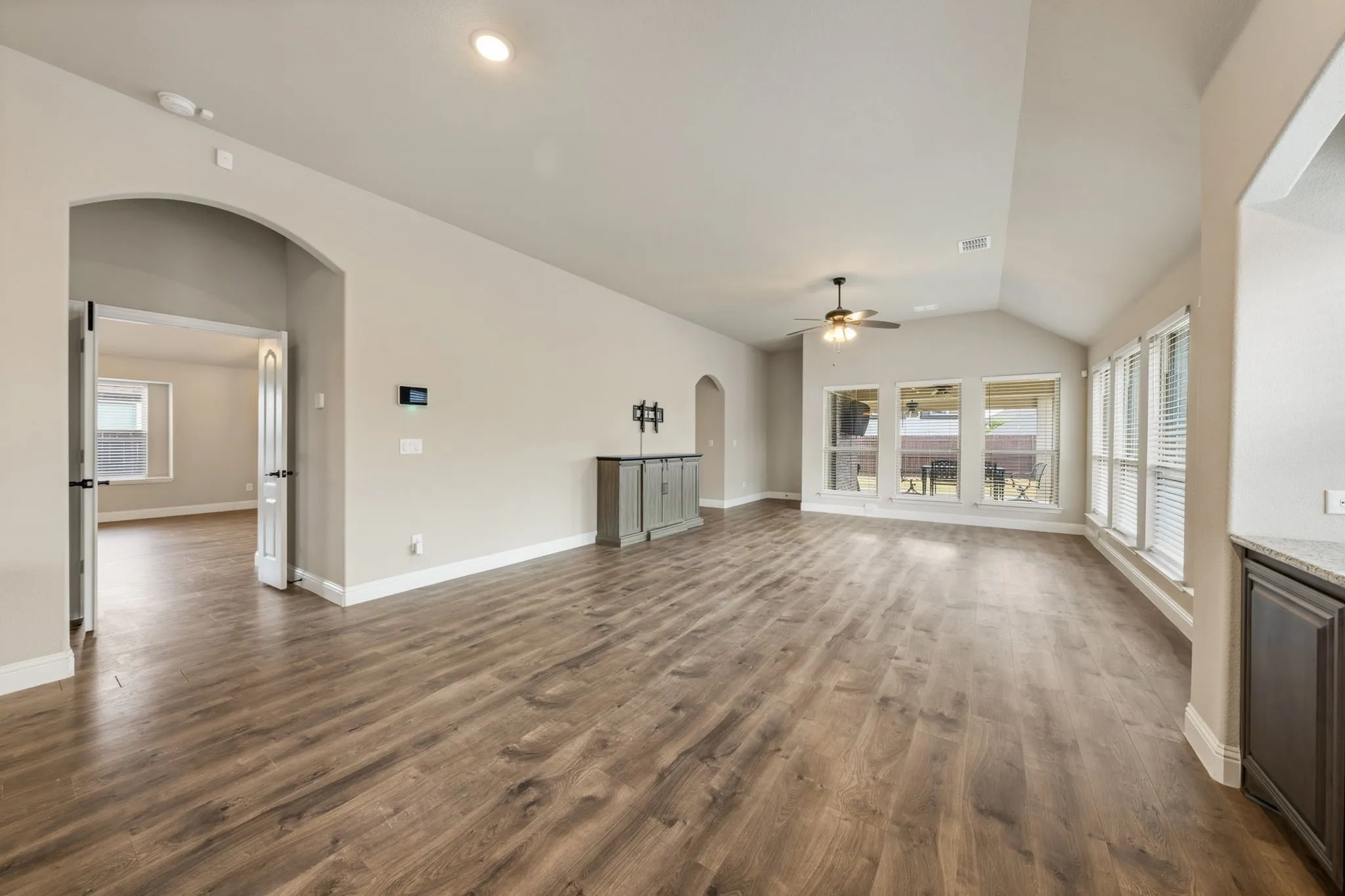 Vaulted ceiling with a ceiling fan, wood-finish flooring, arched doorway, and a wall of windows