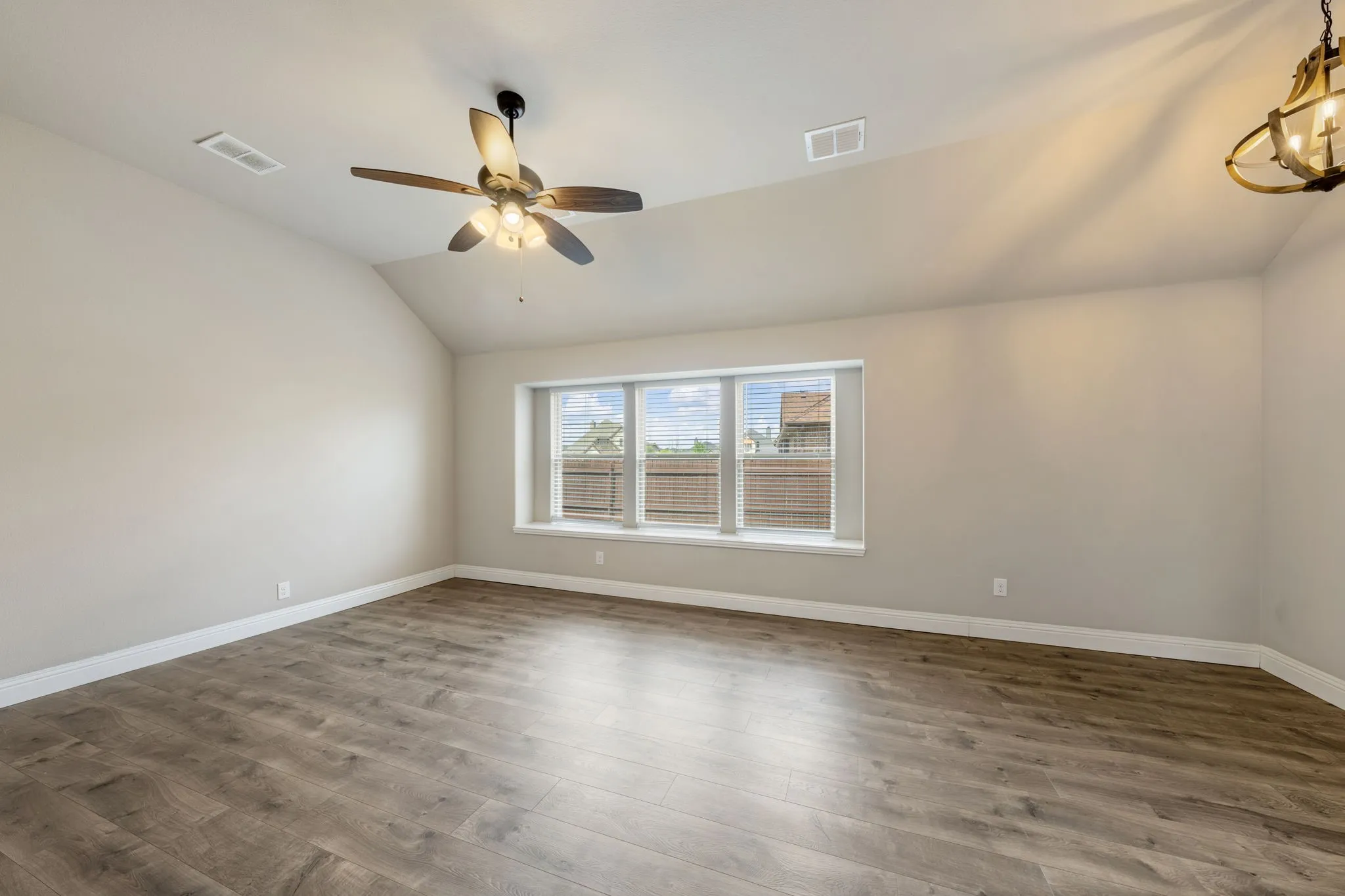 Vaulted ceiling with a ceiling fan, wood-finish flooring, and a large window with privacy blinds
