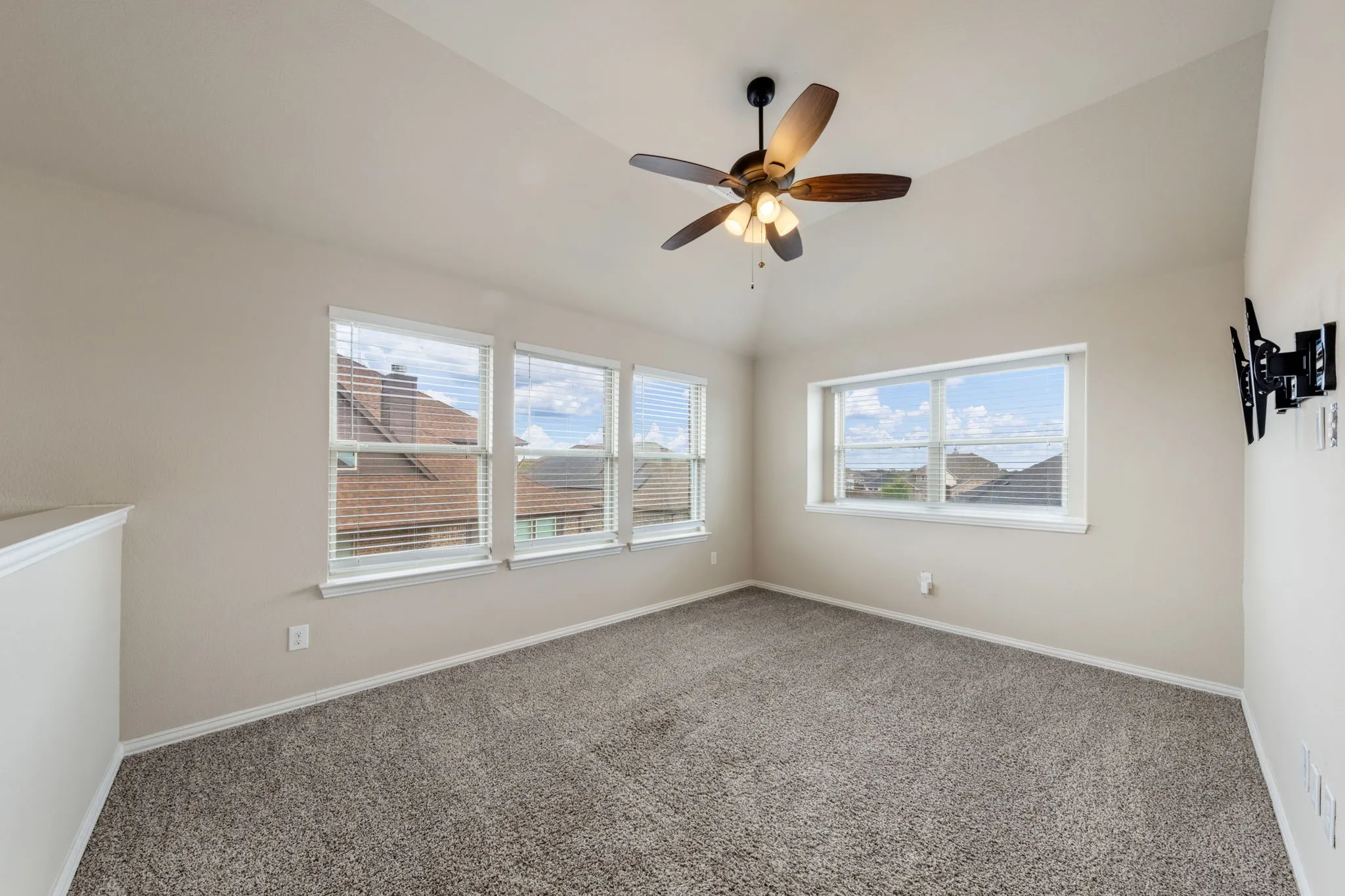 Vaulted ceiling with a ceiling fan, multiple windows with blinds, neutral carpet, and a wall-mounted bracket